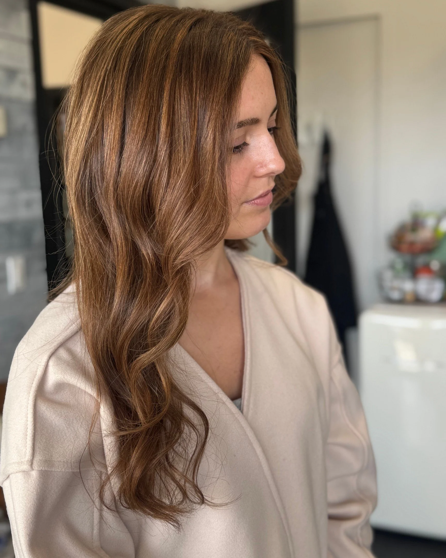 A woman with long, wavy, reddish-brown hair looking down in a kitchen or domestic setting.