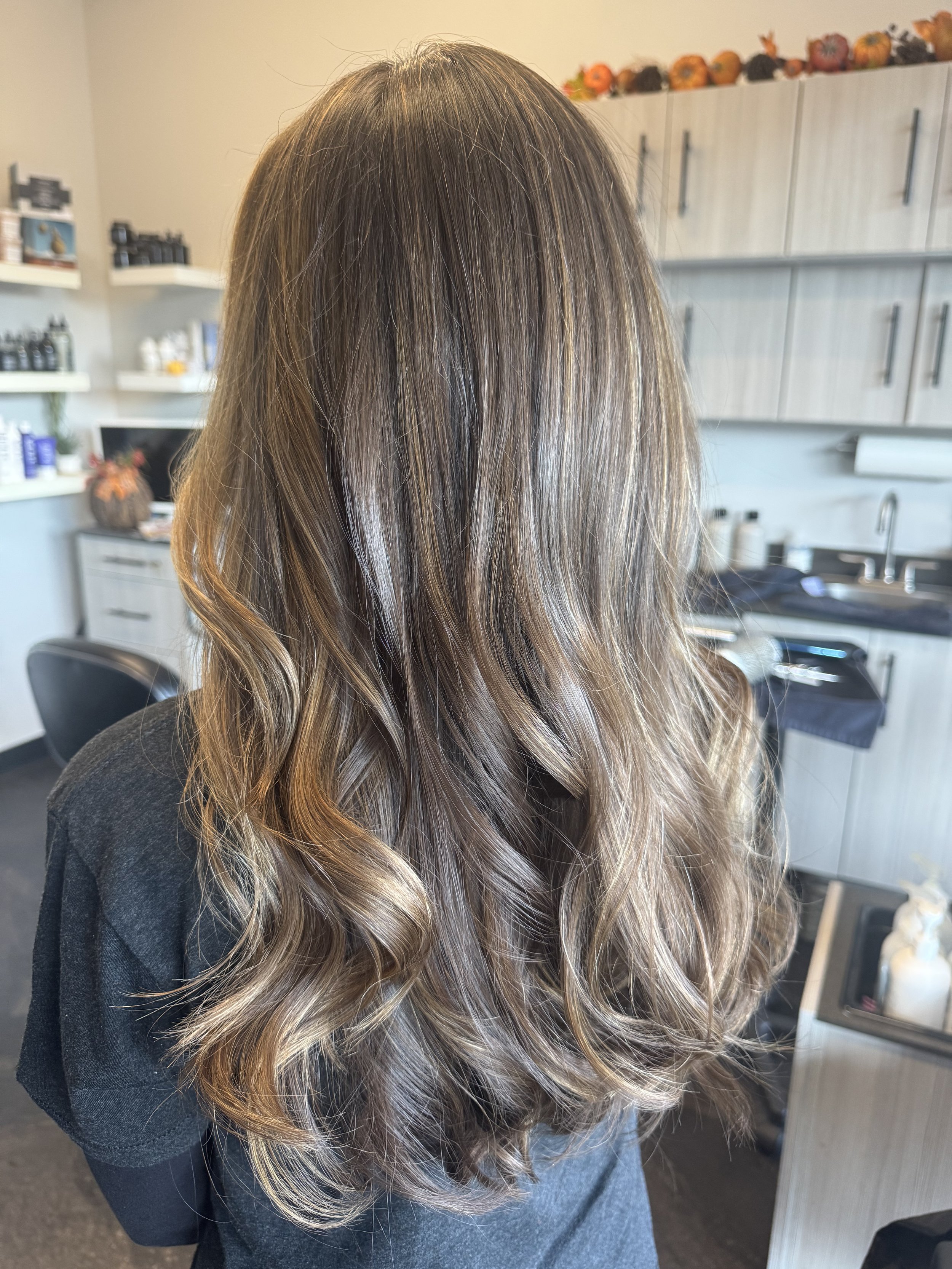 Back view of woman with long, wavy, light brown hair in a salon setting.
