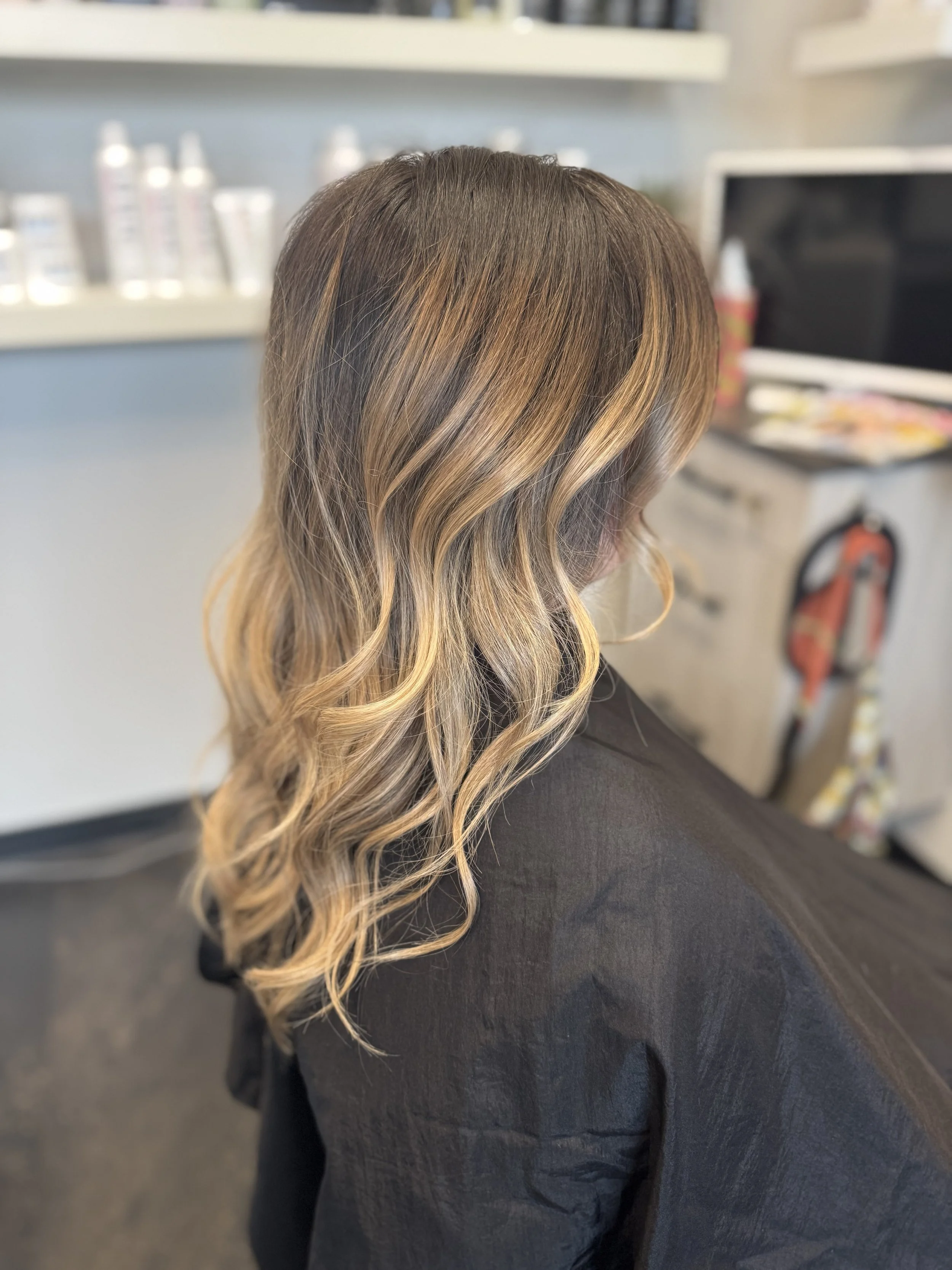 Woman with wavy, blonde balayage hair sitting in a salon.