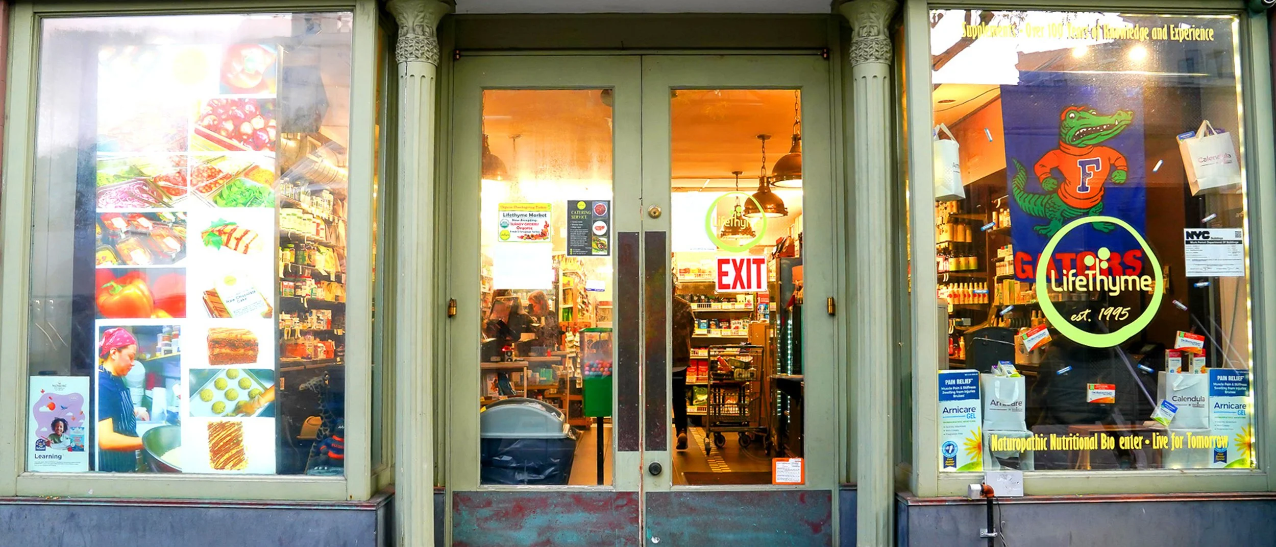 Exterior view of a LifeThyme Natural Health Food store with glass doors, side windows displaying product advertisements in Greenwich Village, New York.