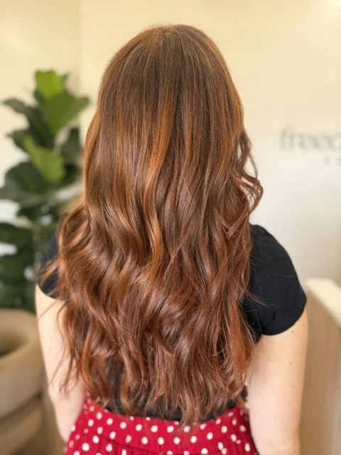 Back view of a woman with long, wavy, red hair in a luxury hair salon.