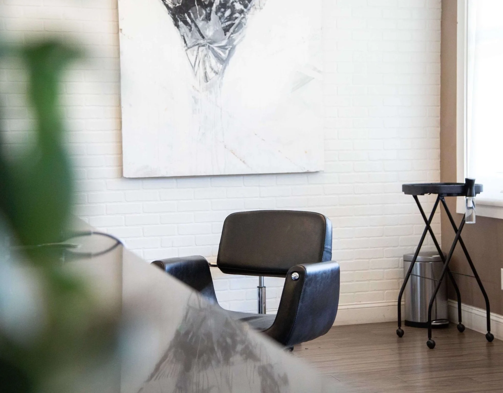 Empty black office chair in a modern office space with white brick wall, abstract artwork, and a rolling cart