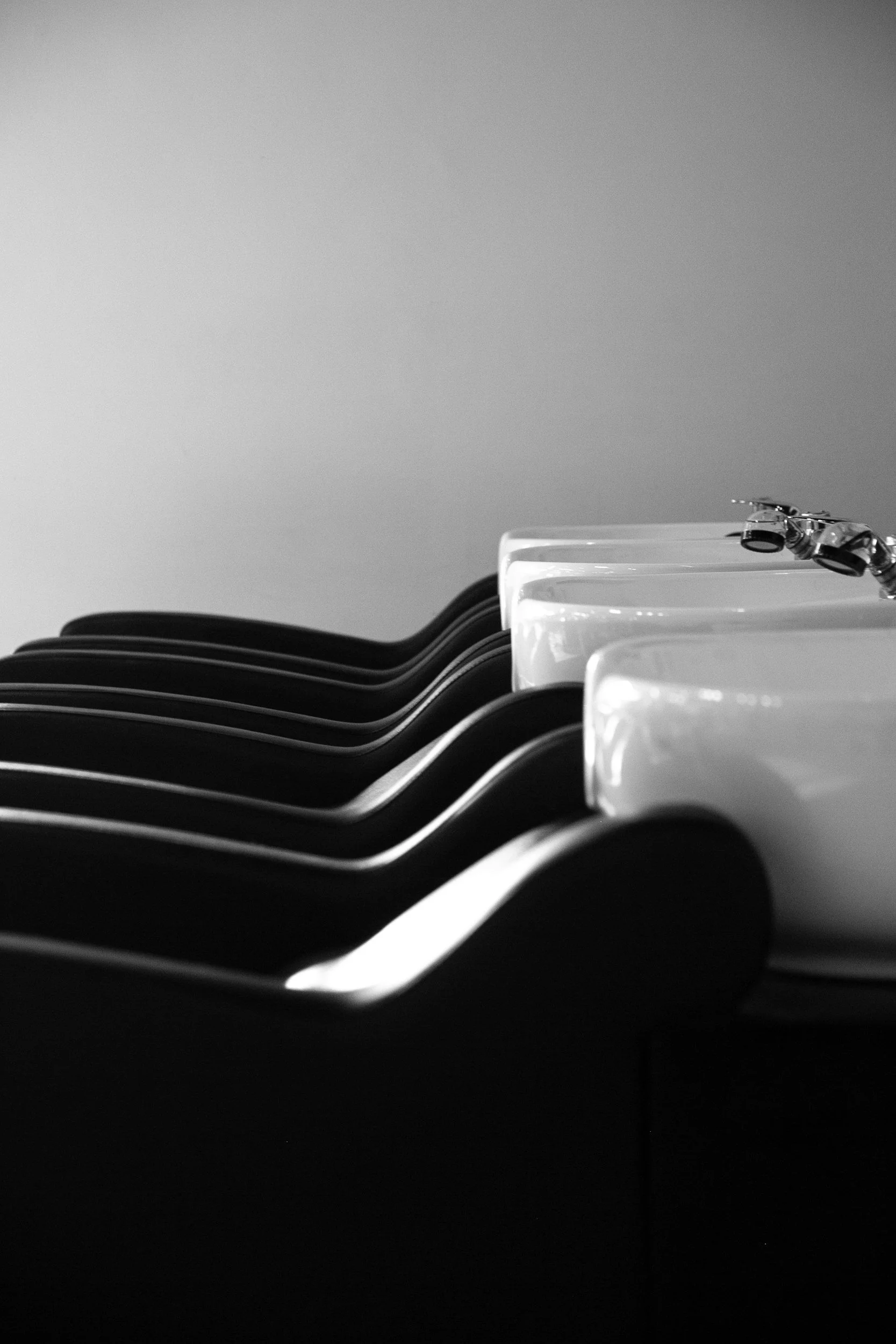 Black and white photo of a row of sinks with faucets in a minimalist setting.