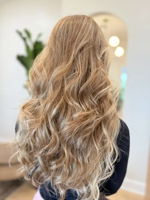 Back view of a woman with long, wavy, blonde hair in a luxury hair salon.