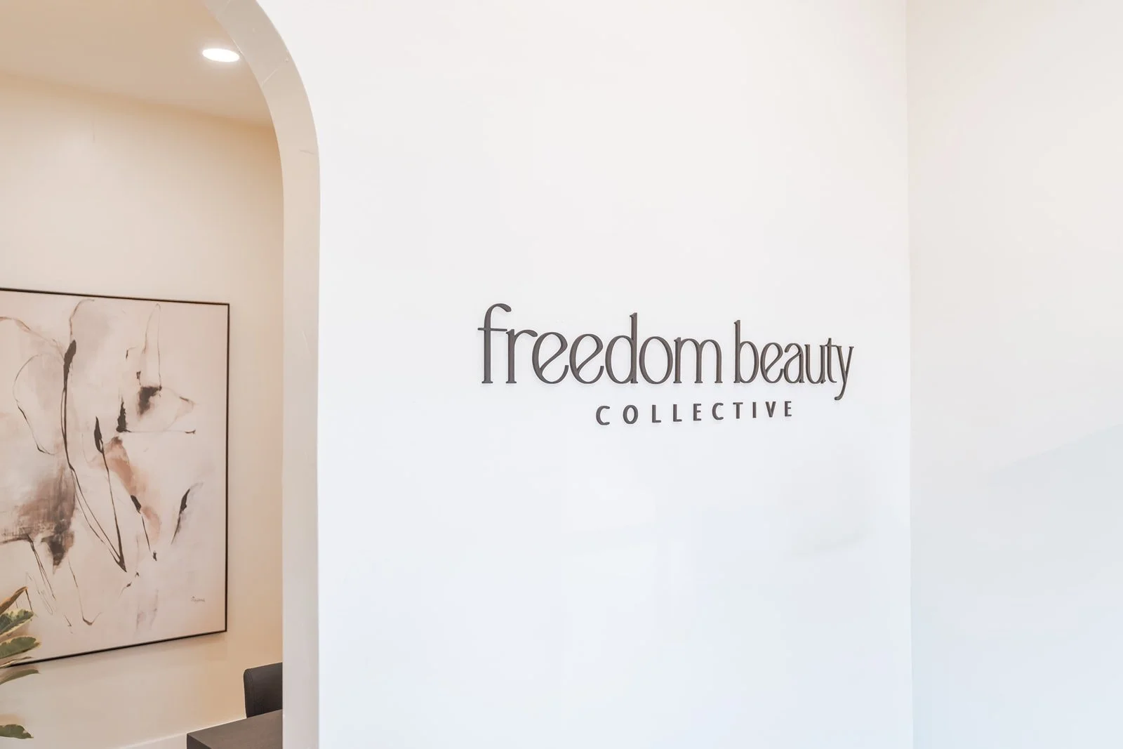 Interior of a beauty salon with a white wall displaying the logo 'freedom beauty COLLECTIVE' and an abstract artwork on the left.