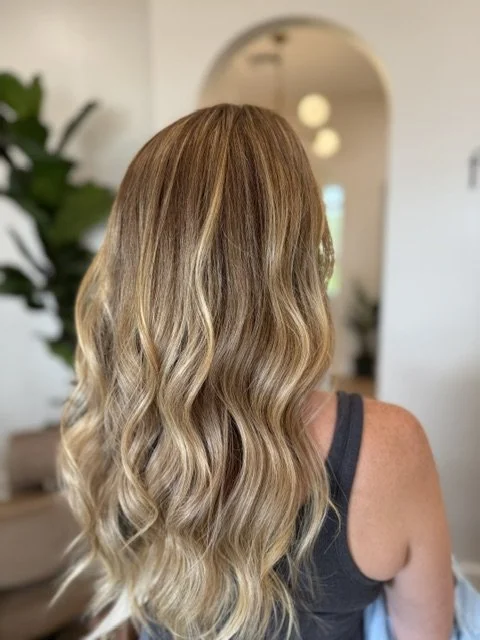 Back view of a woman with long, wavy blonde hair, in a luxury hair salon.
