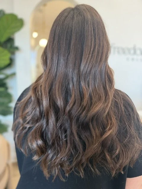 Back view of a woman with long wavy brown hair in a luxury hair salon
