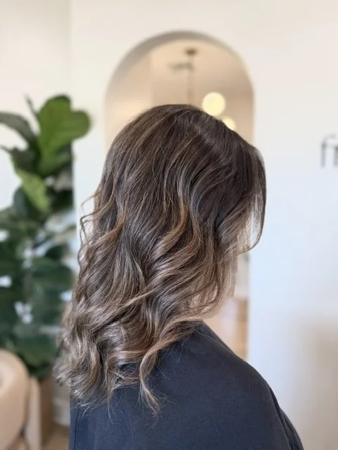 Side view of a woman with shoulder-length, wavy brown hair with highlights in a luxury hair salon.