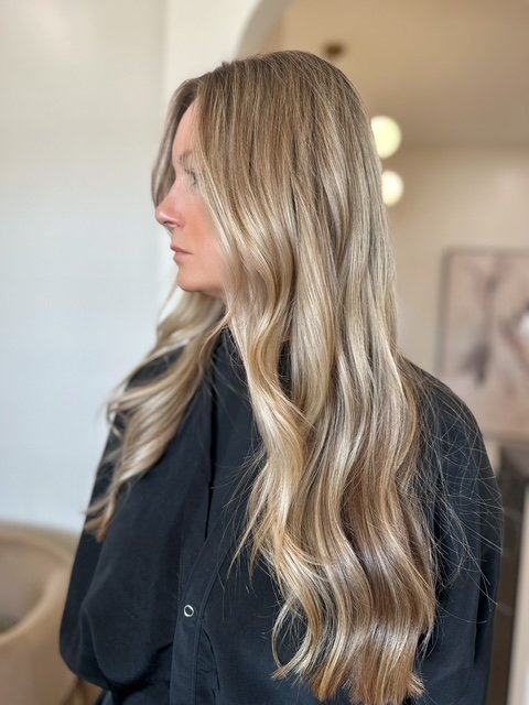 Side profile of a woman with long, wavy blonde hair wearing a black shirt in a room with soft lighting.