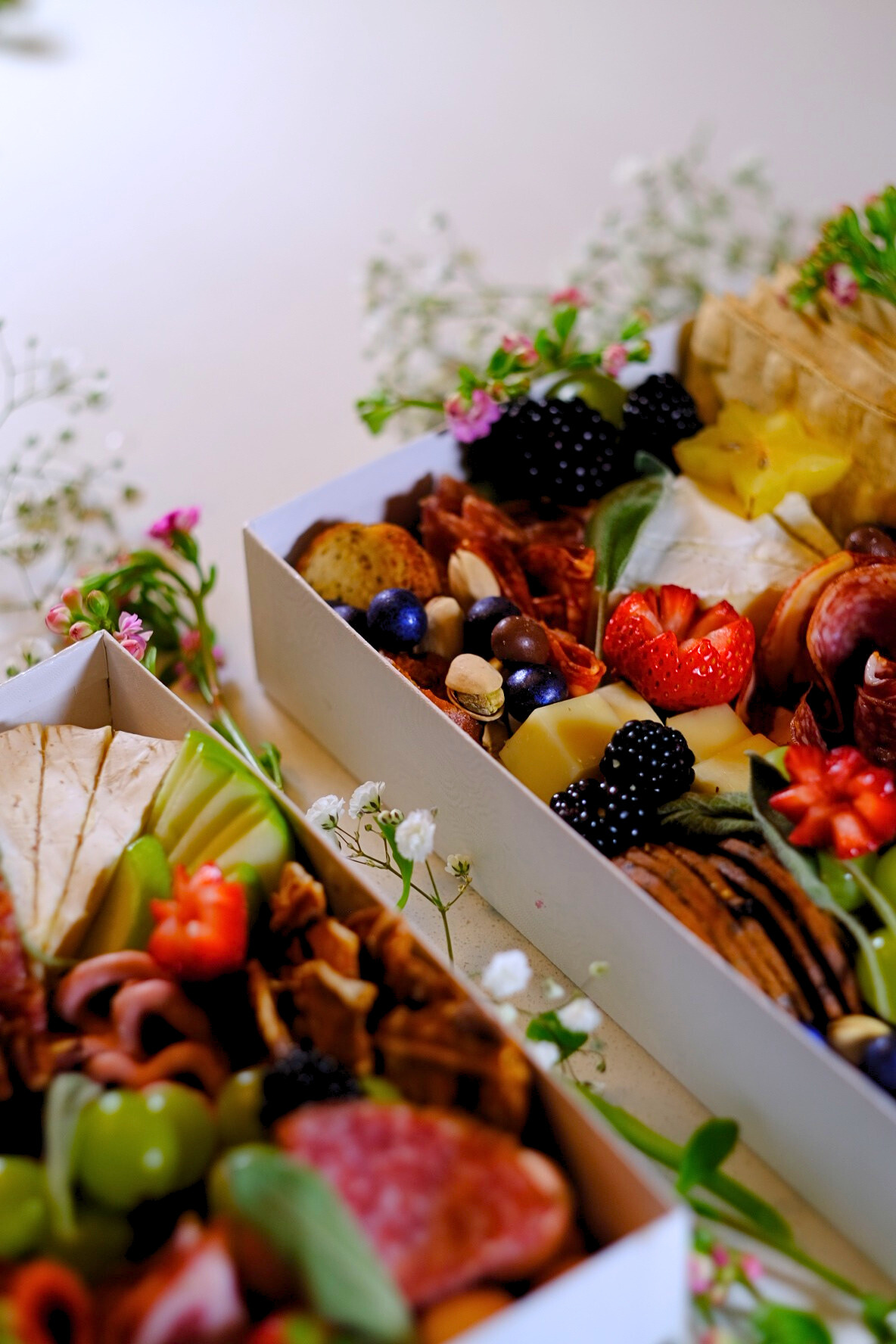Close-up of a cheese and fruit platter with strawberries, blackberries, blueberries, grapes, and various cheeses, arranged with flowers around the edges.
