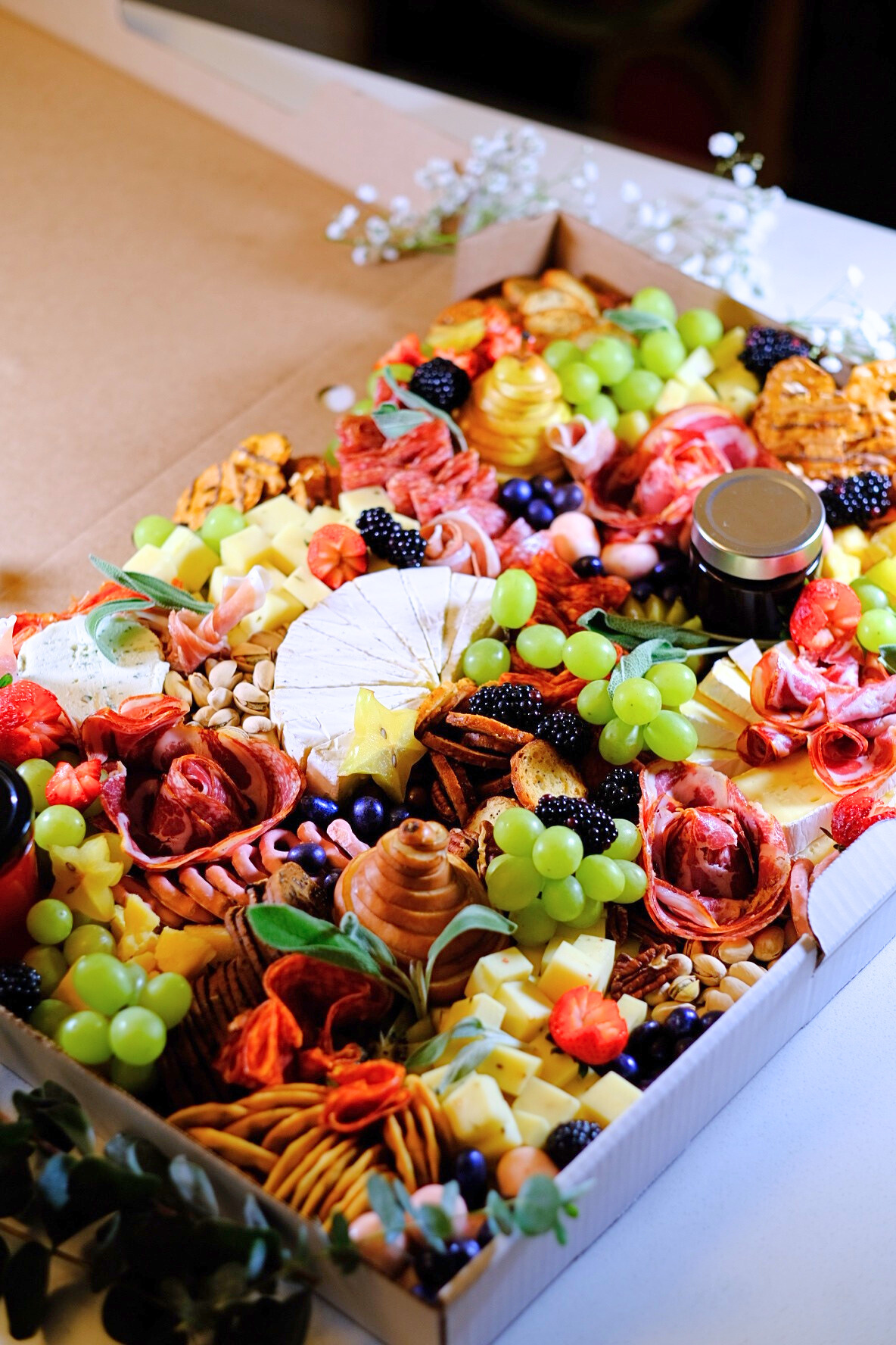 A large cheese and charcuterie board with grapes, blackberries, crackers, nuts, cheeses, meats, and decorative flowers.