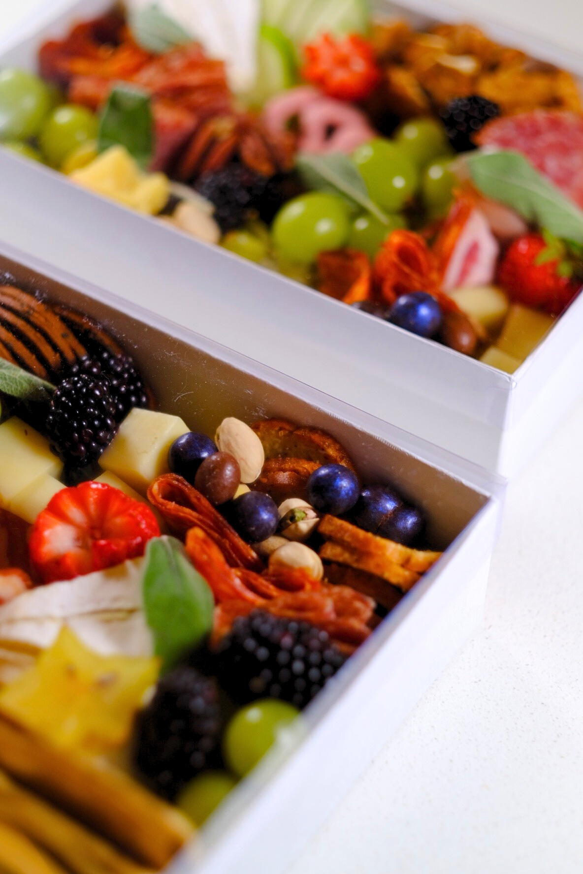 Box with assorted fresh fruit including strawberries, blackberries, blueberries, grapes, pineapple, and nuts.