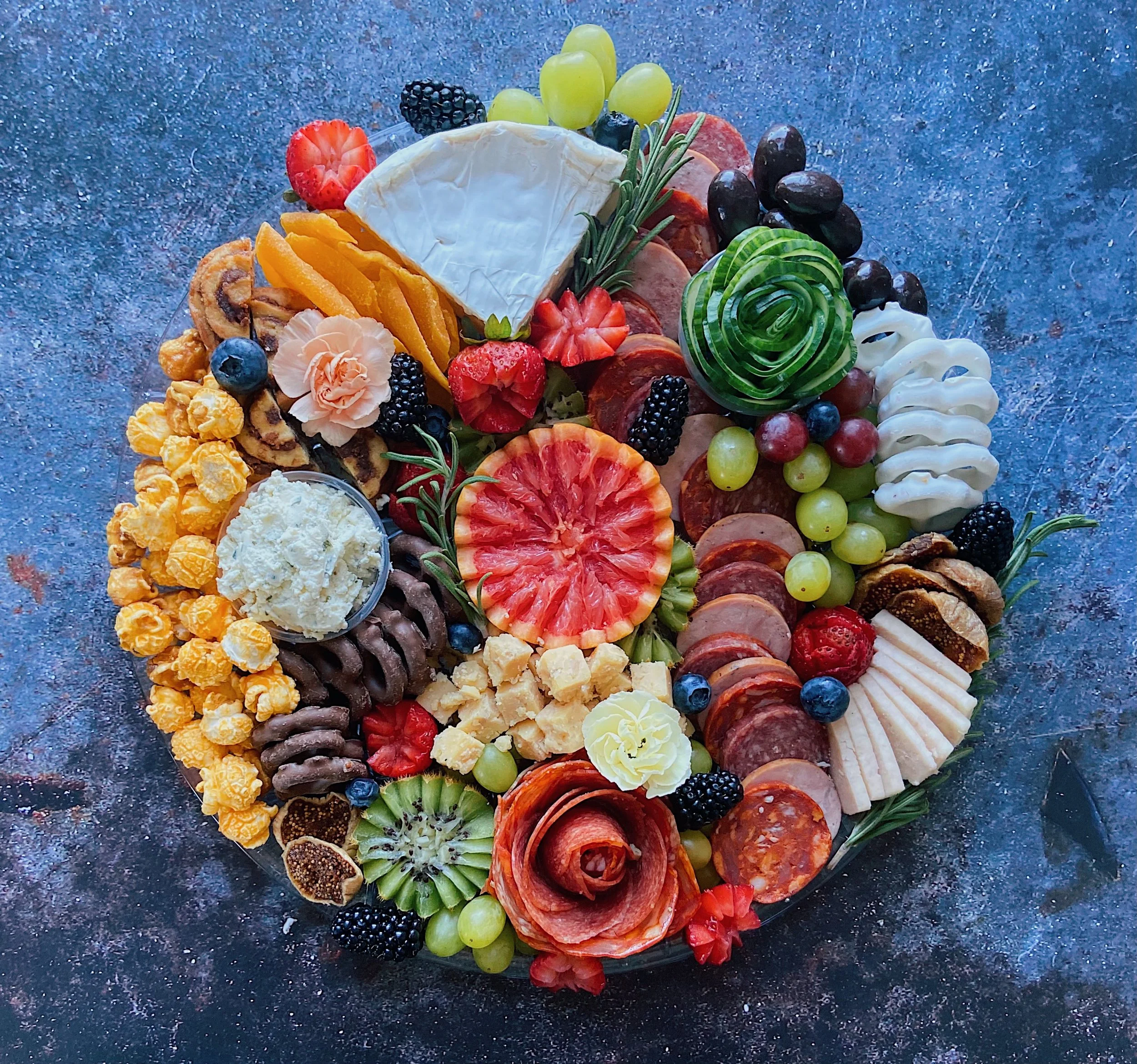 Charcuterie board with cheese, meats, fruits, crackers, and garnishes arranged on a round dish.