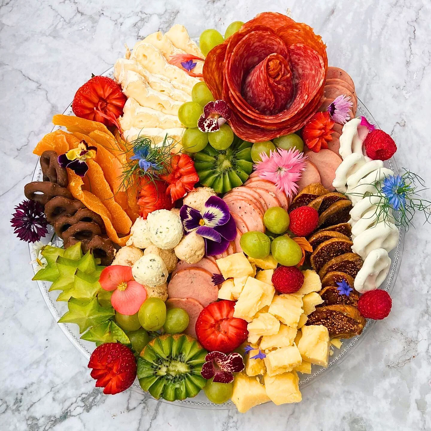 Assorted cheeses, cured meats, fresh fruits, and flowers arranged on a platter