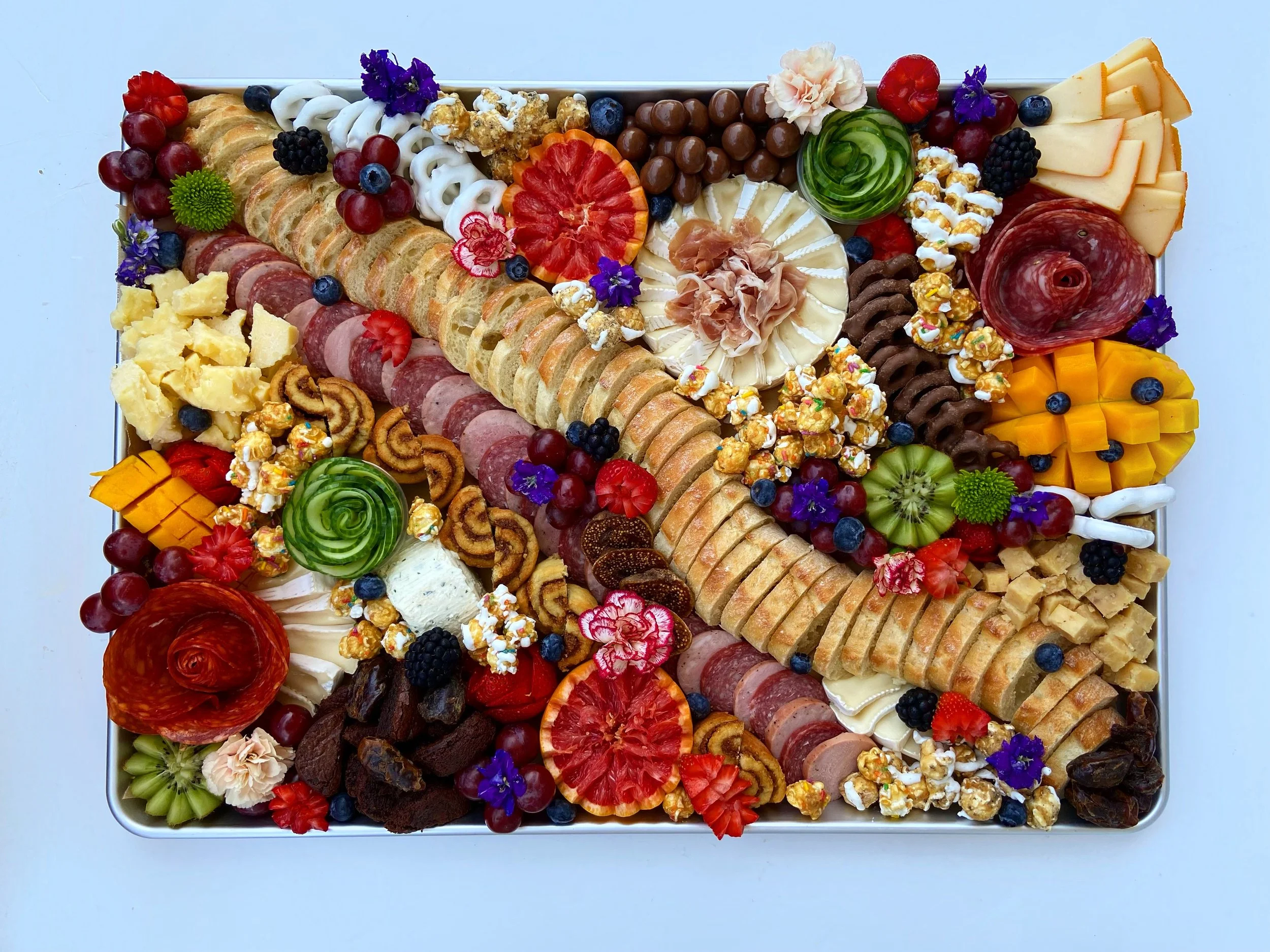 A tray of assorted cheeses, fruits, crackers, chocolates, and candies arranged for a charcuterie board.