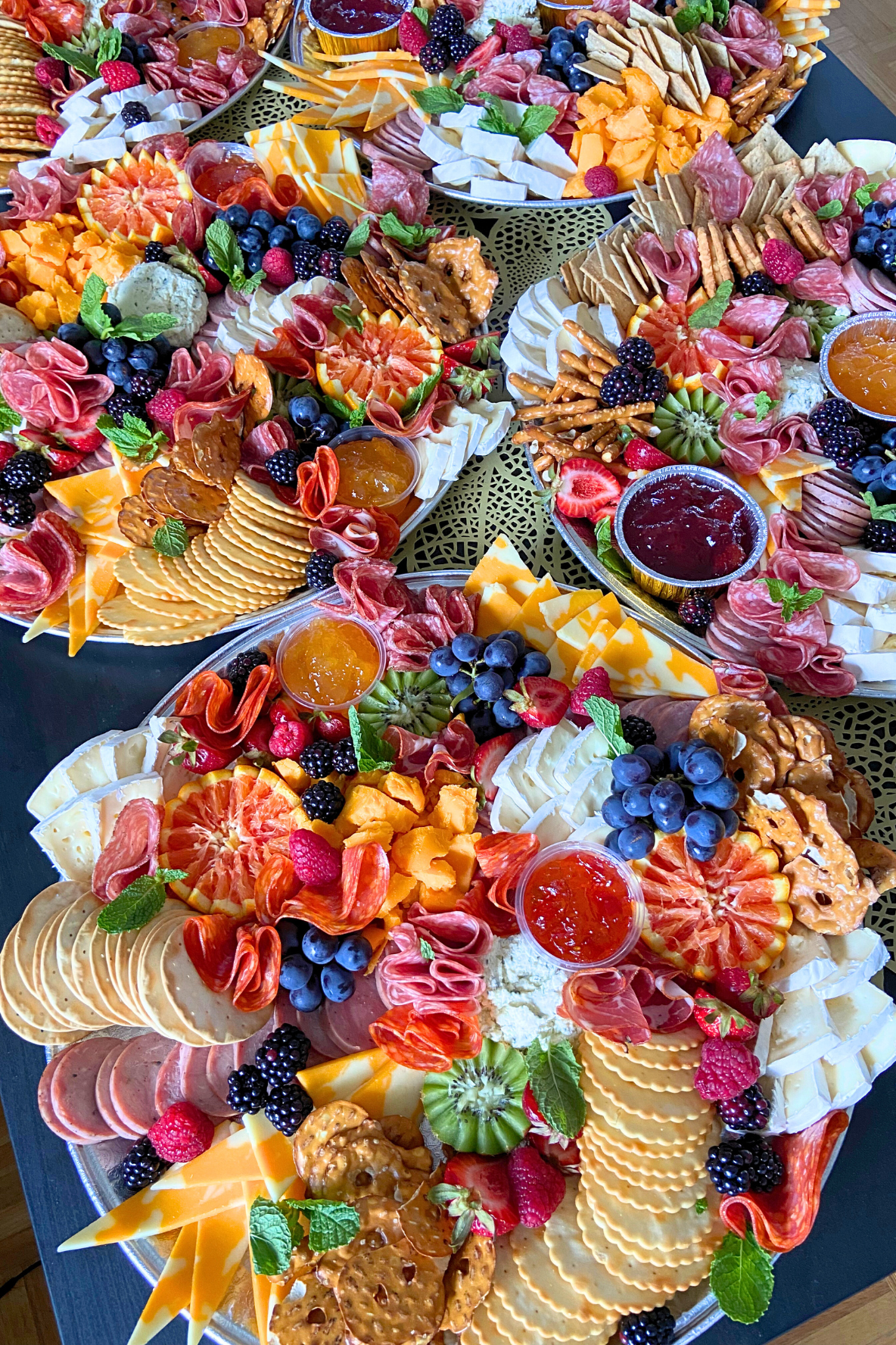 Colorful fruit and cheese charcuterie boards with strawberries, blueberries, blackberries, raspberries, oranges, grapes, various cheeses, crackers, nuts, honey, and mint leaves.
