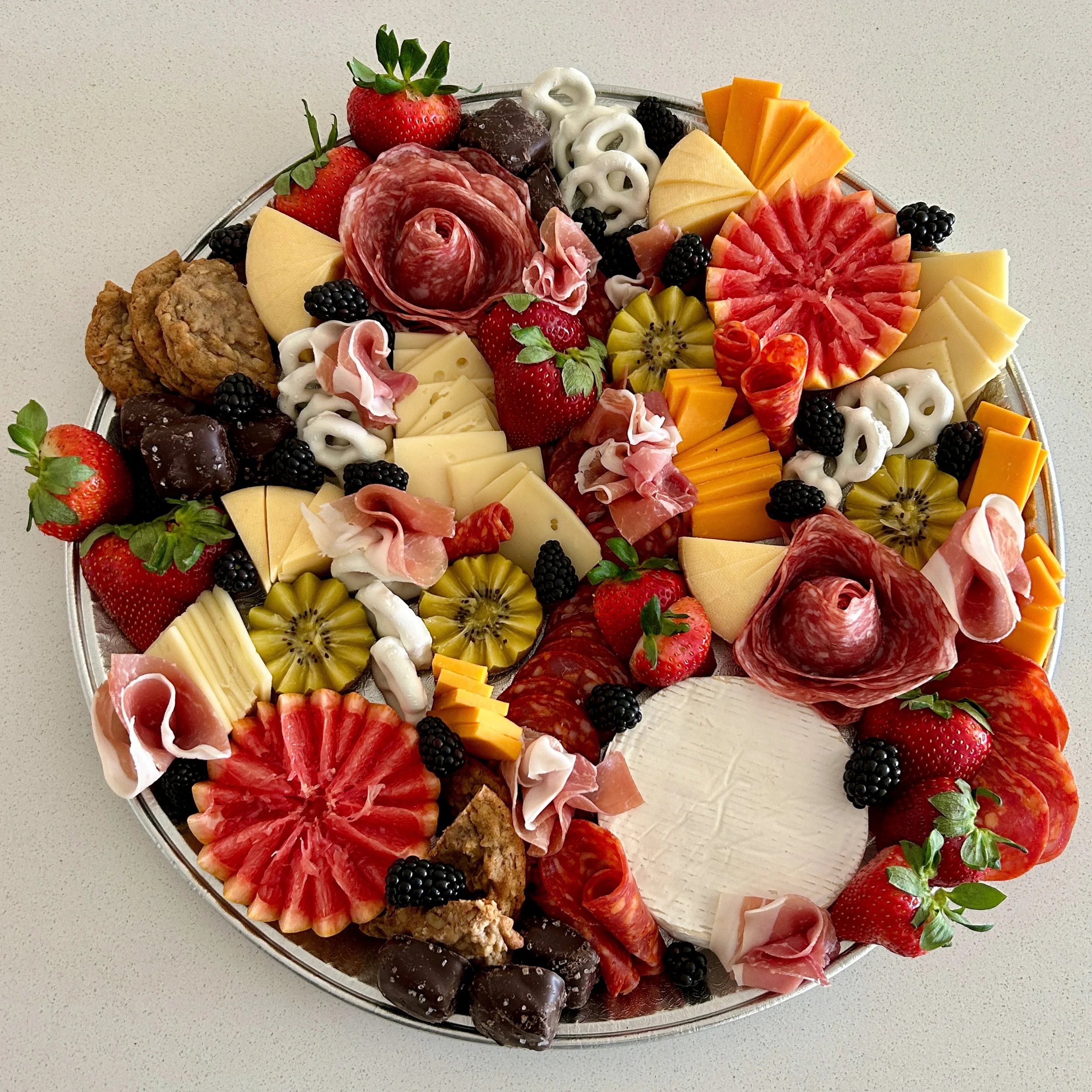 Charcuterie board with strawberries, blackberries, sliced kiwis, orange and yellow cheeses, cured meats, crackers, and chocolates.
