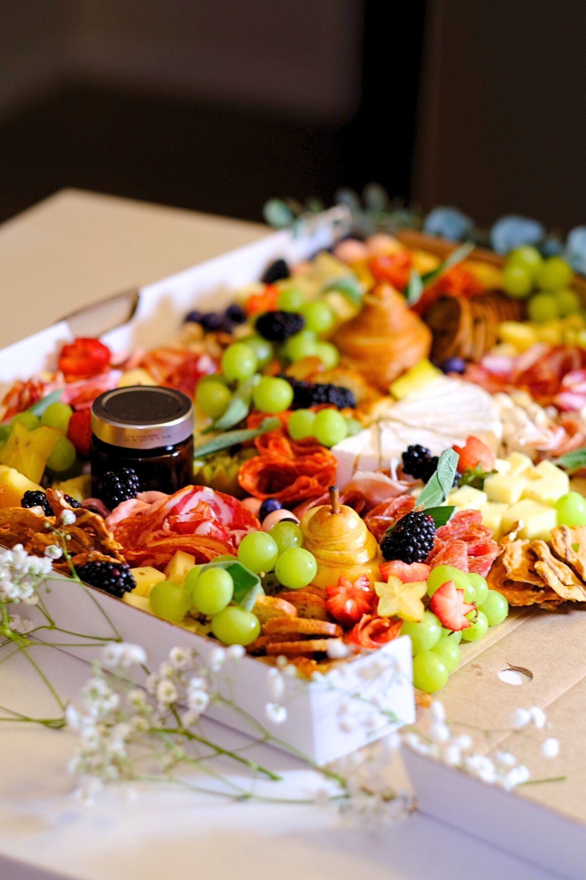 A tray of assorted cheese, grapes, blackberries, dried fruit, and cut strawberries for a charcuterie board.