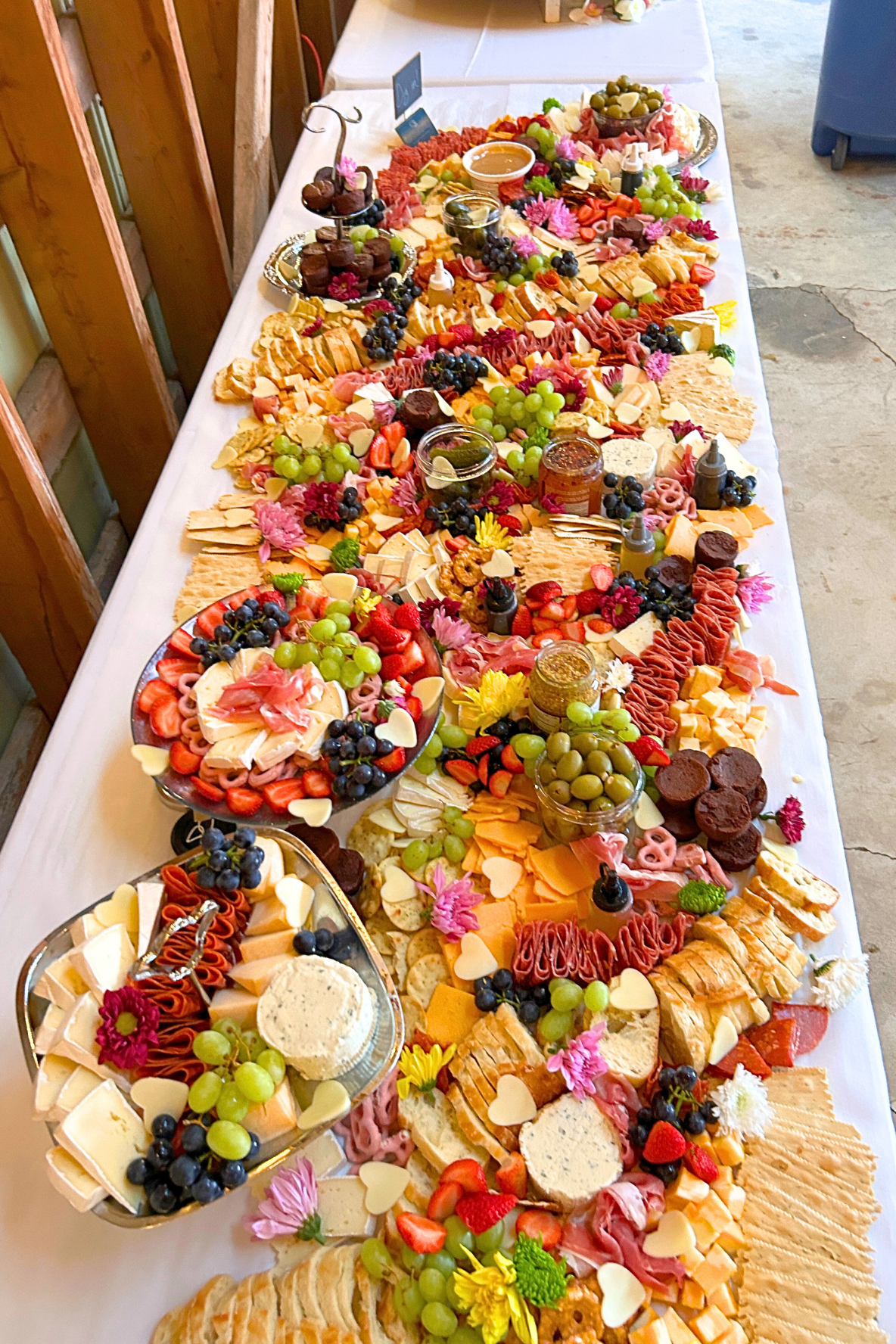 A large charcuterie and cheese platter filled with assorted cheeses, grapes, strawberries, crackers, meats, dips, and garnished with flowers.