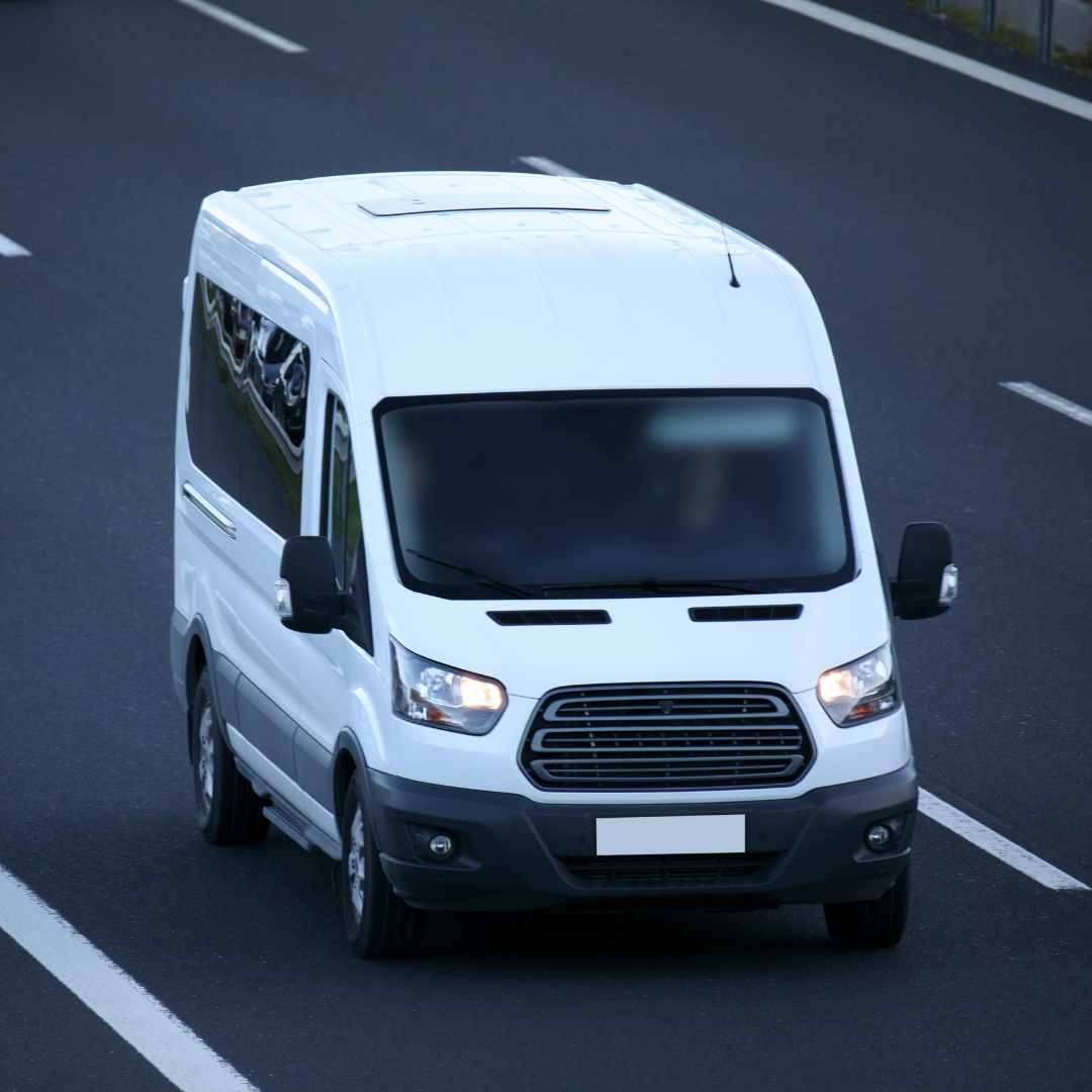 A white cargo van driving on a highway with marked lanes.