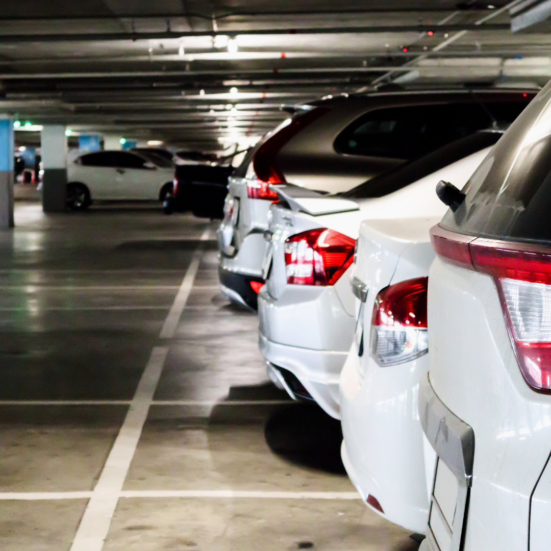 A row of parked cars in an indoor parking garage, with overhead lights and concrete columns visible.