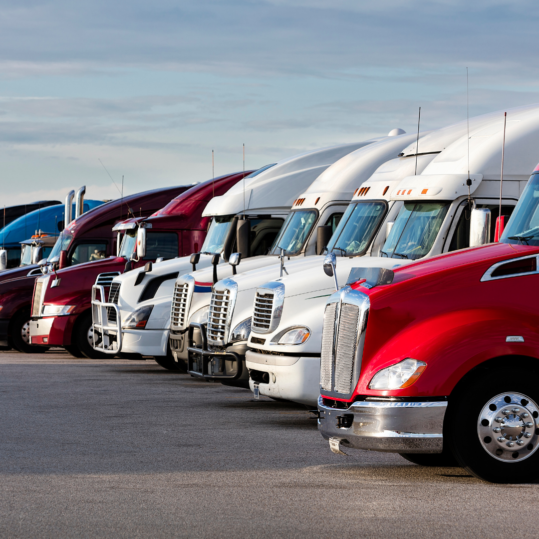 A row of semi-trucks parked in a lot under a cloudy sky.