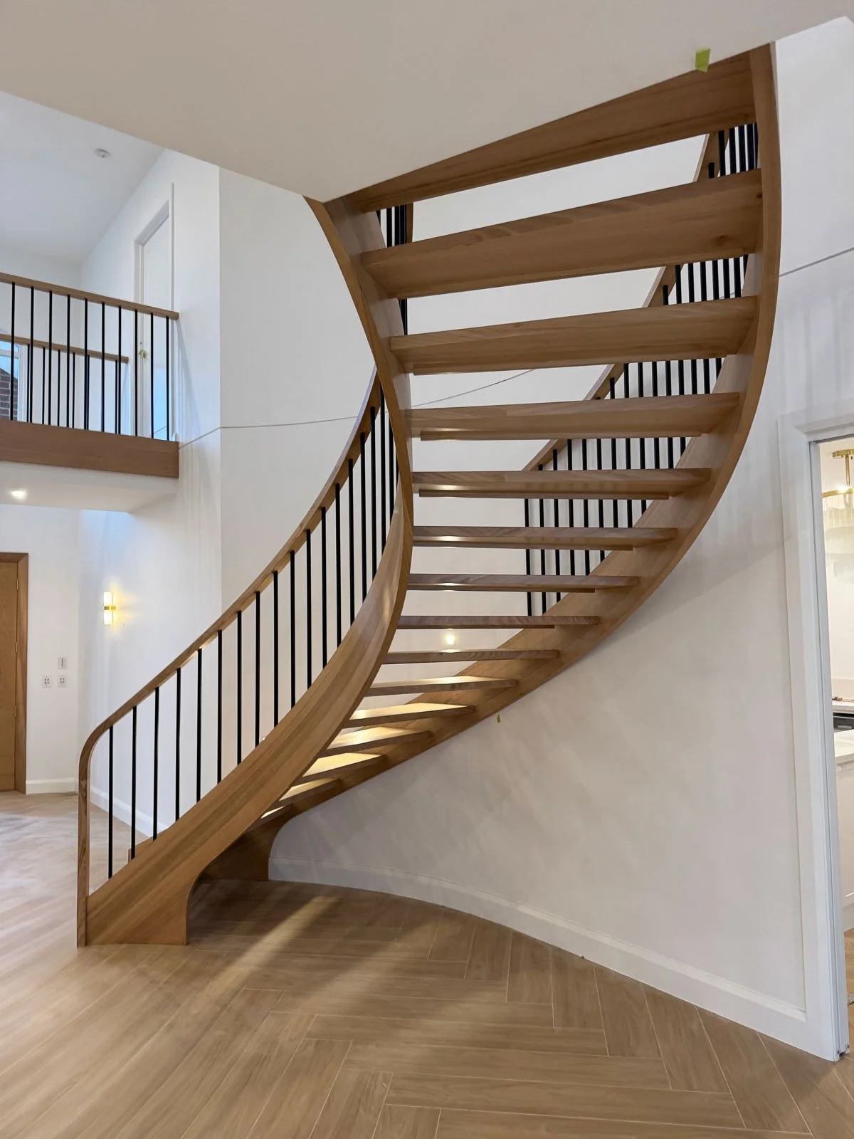 Interior view of a curved wooden staircase with black metal balusters in a modern home. Staircase Polishing Sydney