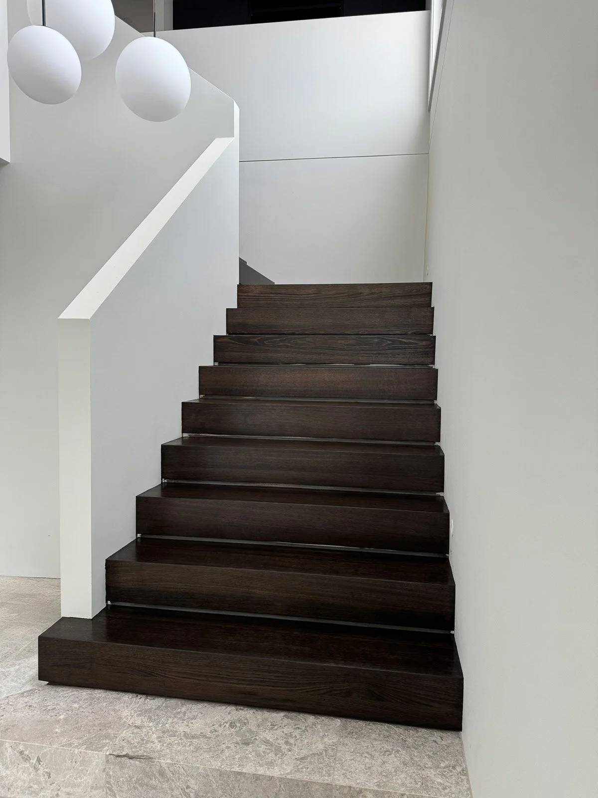 Dark wooden stairs with white walls on either side and a white railing on the left, leading upward to a modern interior space with white walls and a gray ceiling. Staircase Polishing Sydney