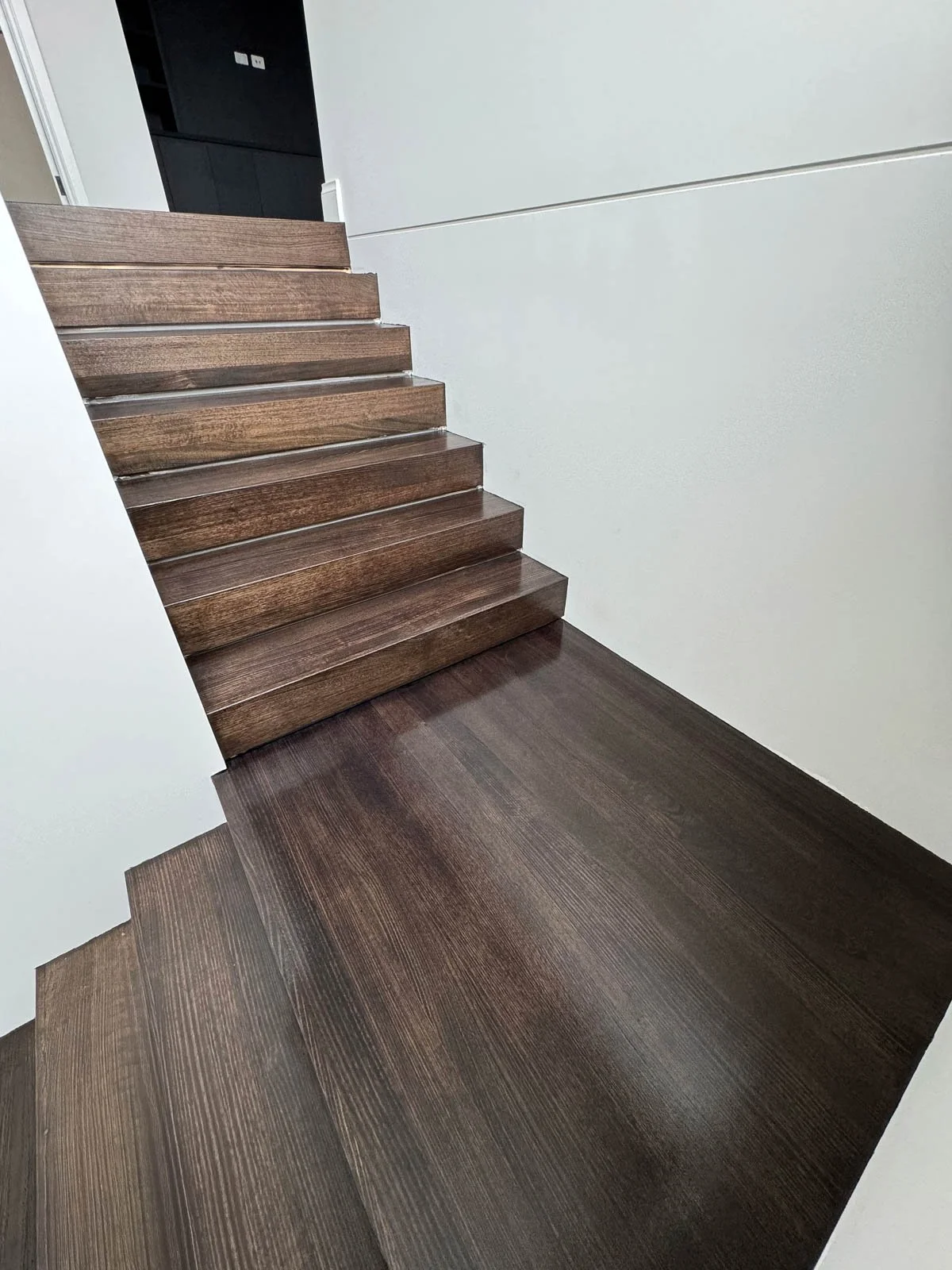 Photo of a staircase with dark wooden steps and matching dark wooden floor, with white walls on either side. Staircase Polishing Sydney