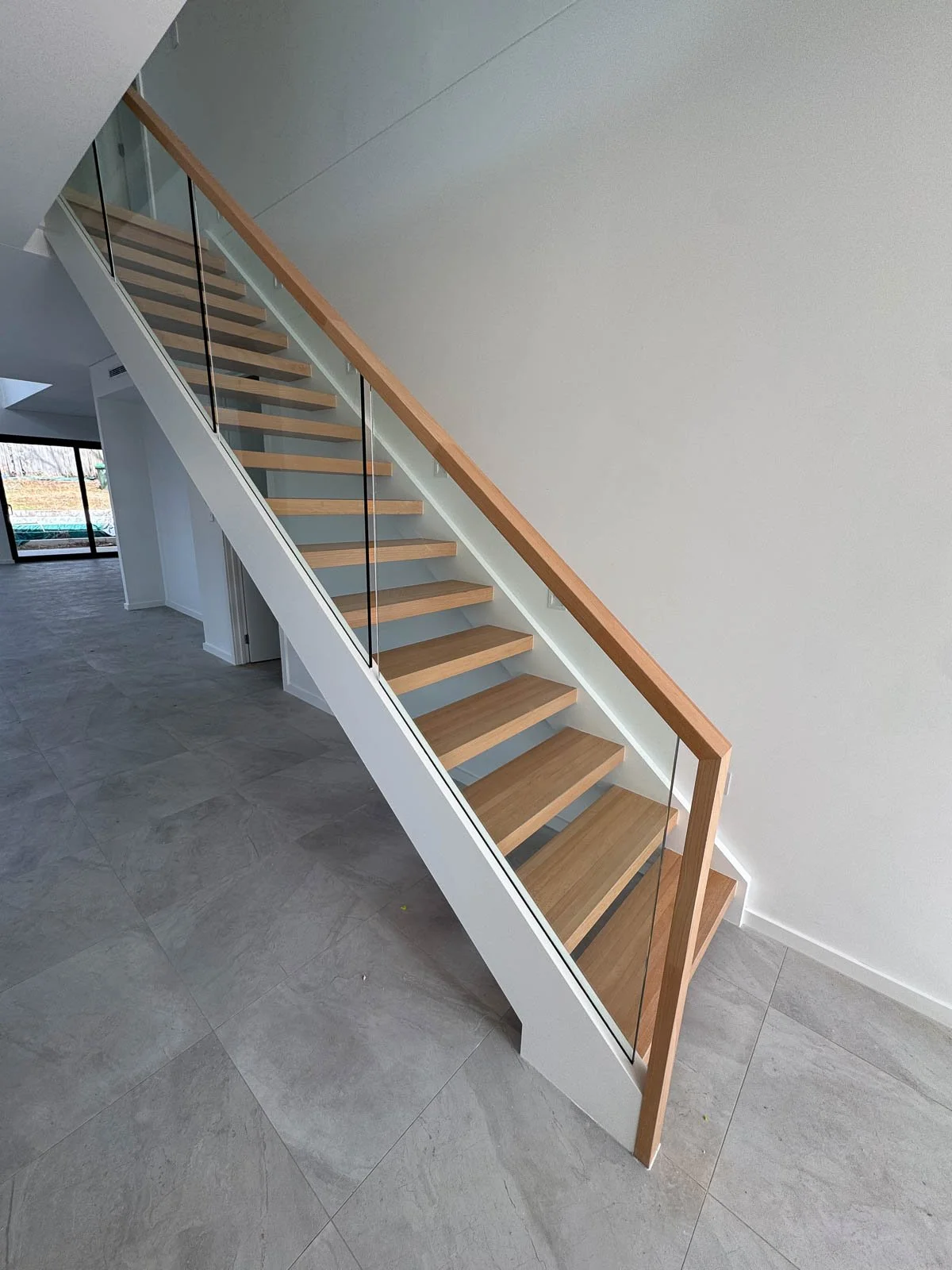 Modern staircase with wooden steps and glass railing in a contemporary home interior. Staircase Polishing Sydney