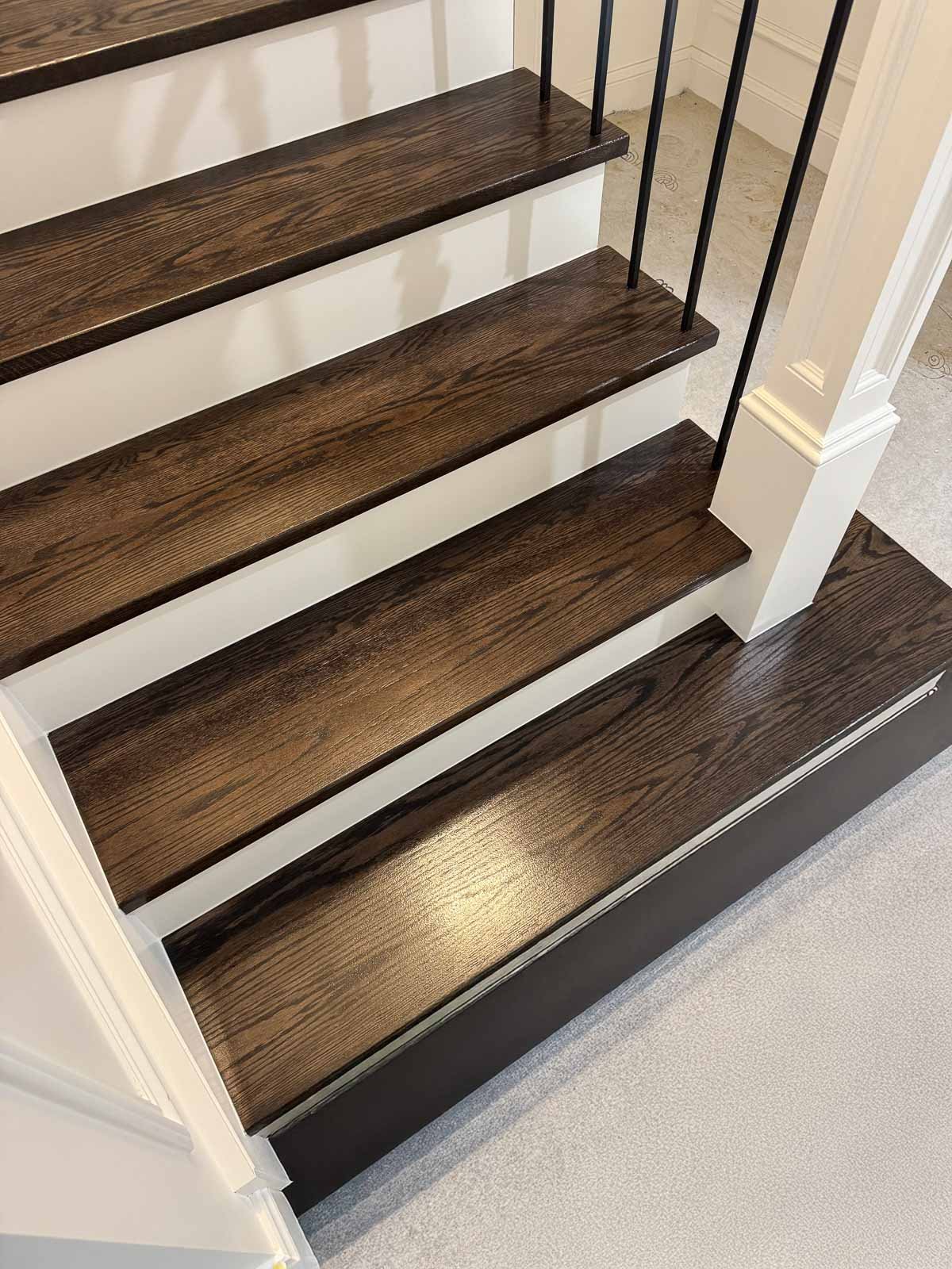Close-up view of a staircase with dark wood steps, white risers, and black metal balusters. Staircase Polishing Sydney