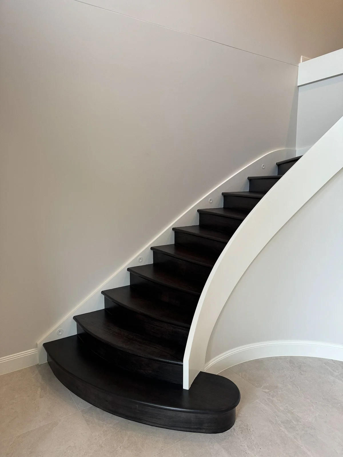 Interior staircase with black wooden steps and a curved white wall. Staircase Polishing Sydney