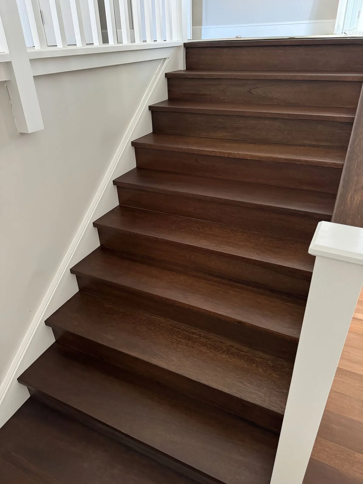 Wooden stairs with white railing and wall.