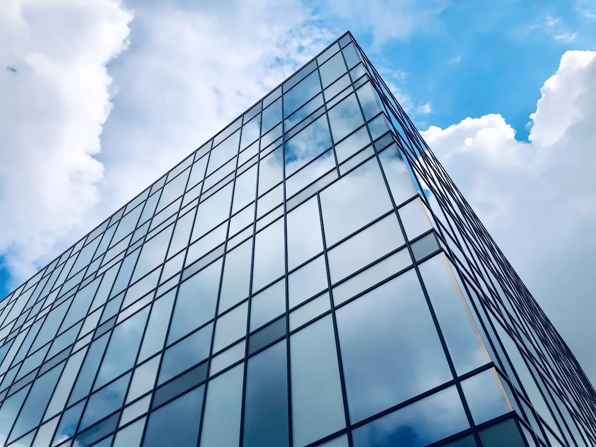 A modern glass office building reflecting the cloudy sky.