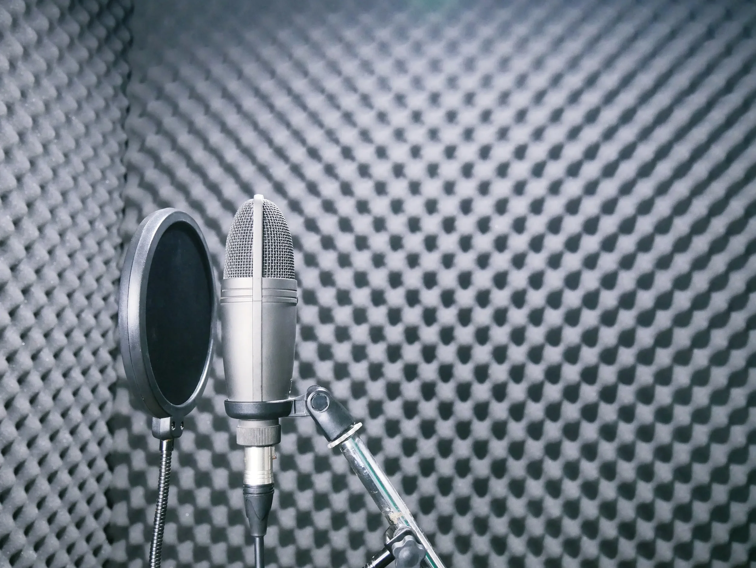 A professional microphone with a pop filter in a recording studio with soundproof foam panels.