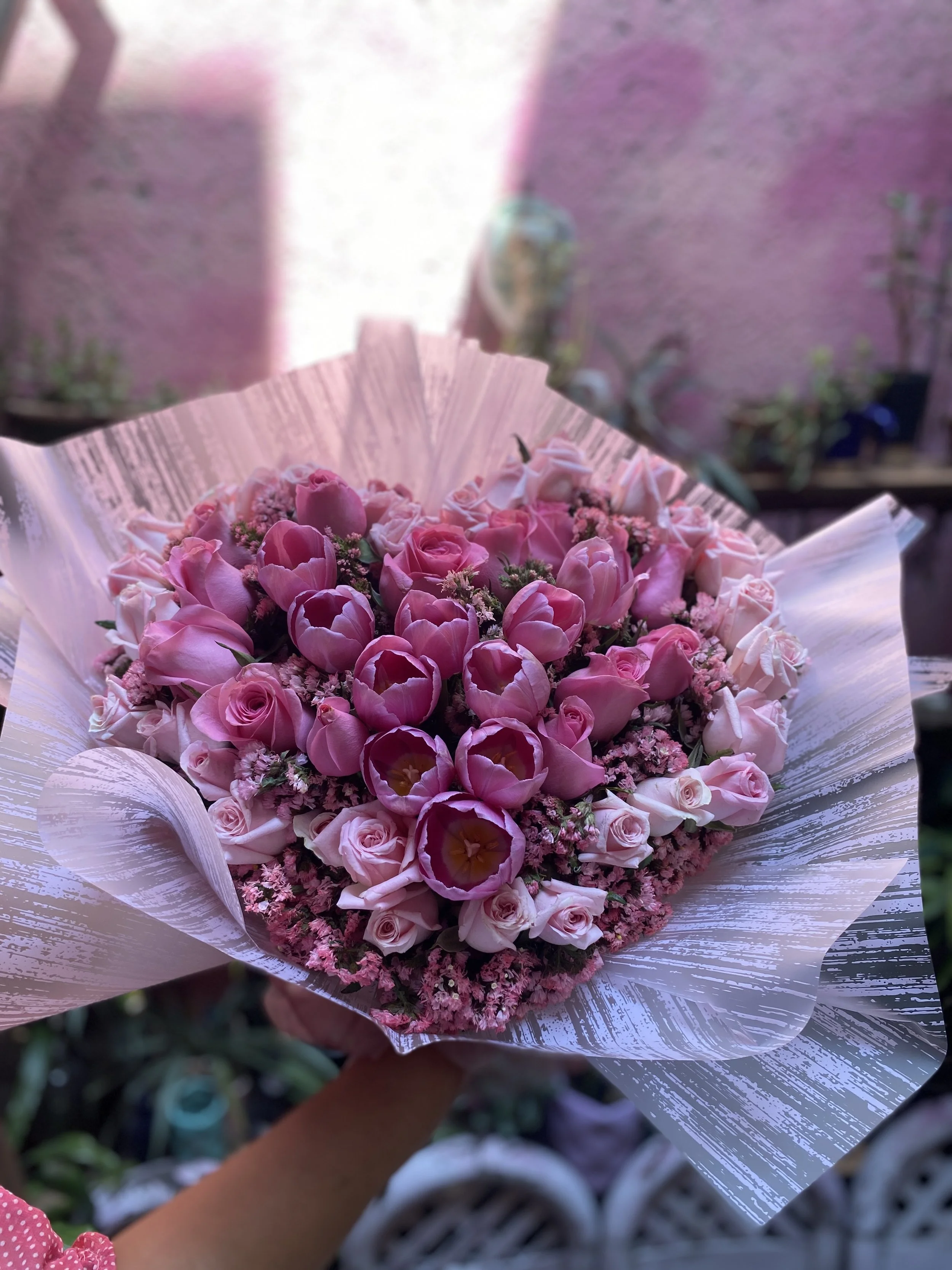 A bouquet of pink roses, tulips, and other flowers wrapped in decorative paper.