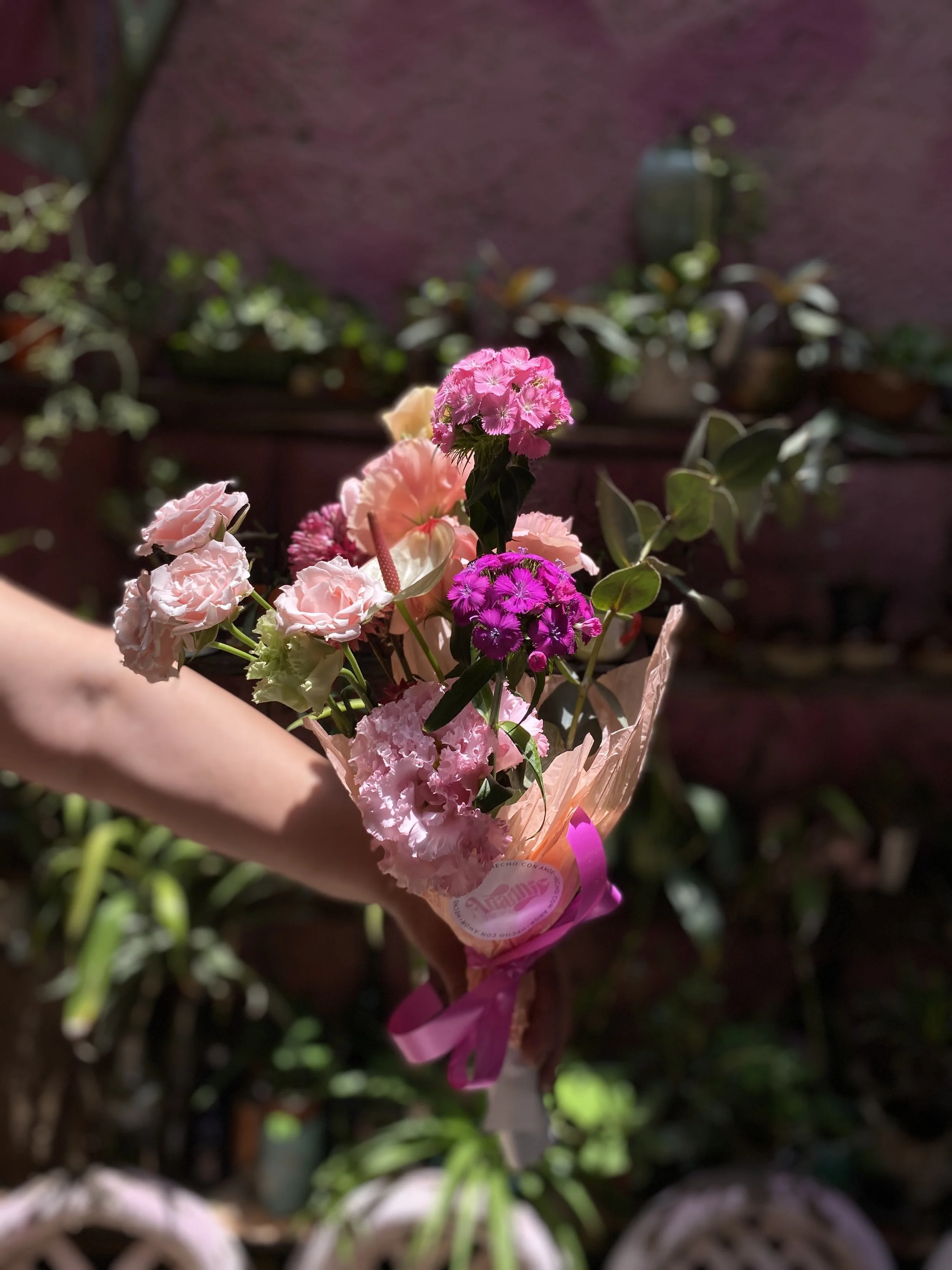 A bouquet of pink, purple, and peach flowers held by a person’s hand with a blurred garden background.