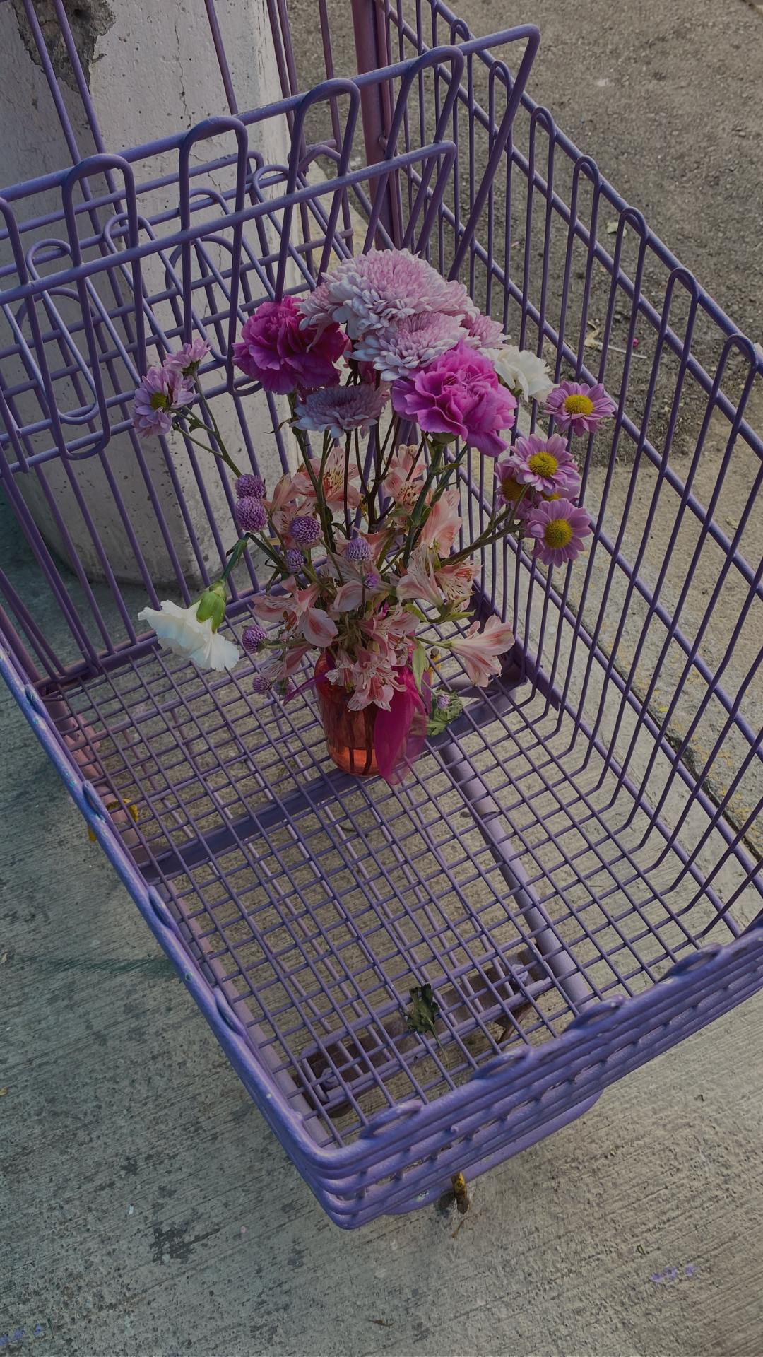 A purple shopping cart with a bouquet of pink, white, and purple flowers in a small brown vase.