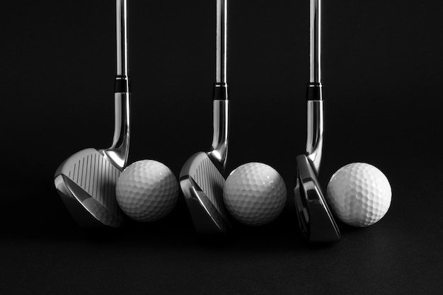 Four golf clubs and four golf balls arranged on a black background.