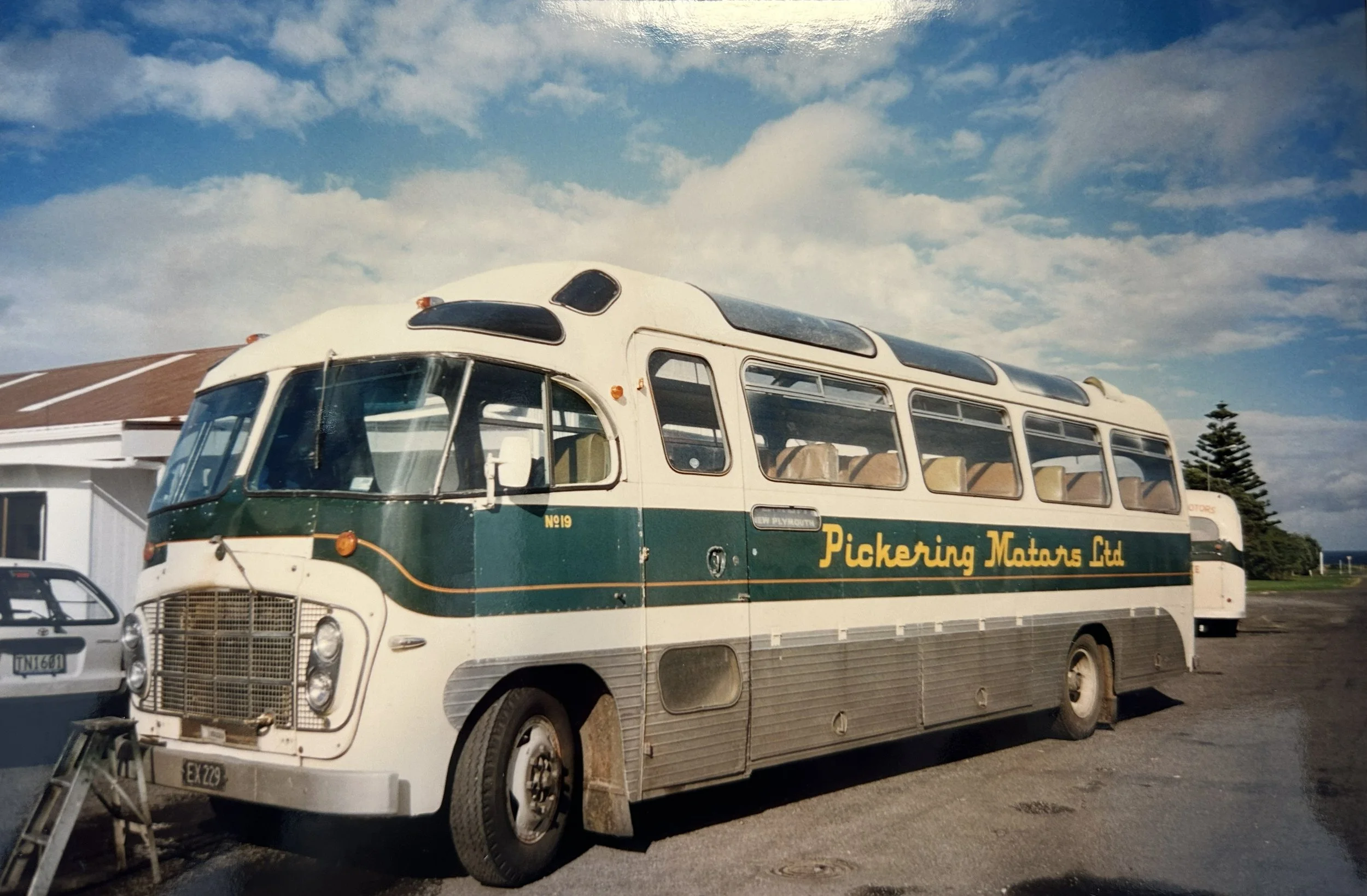Vintage bus labeled 'Pickering Motors Ltd' parked outdoors on a gravel surface under a partly cloudy sky.
