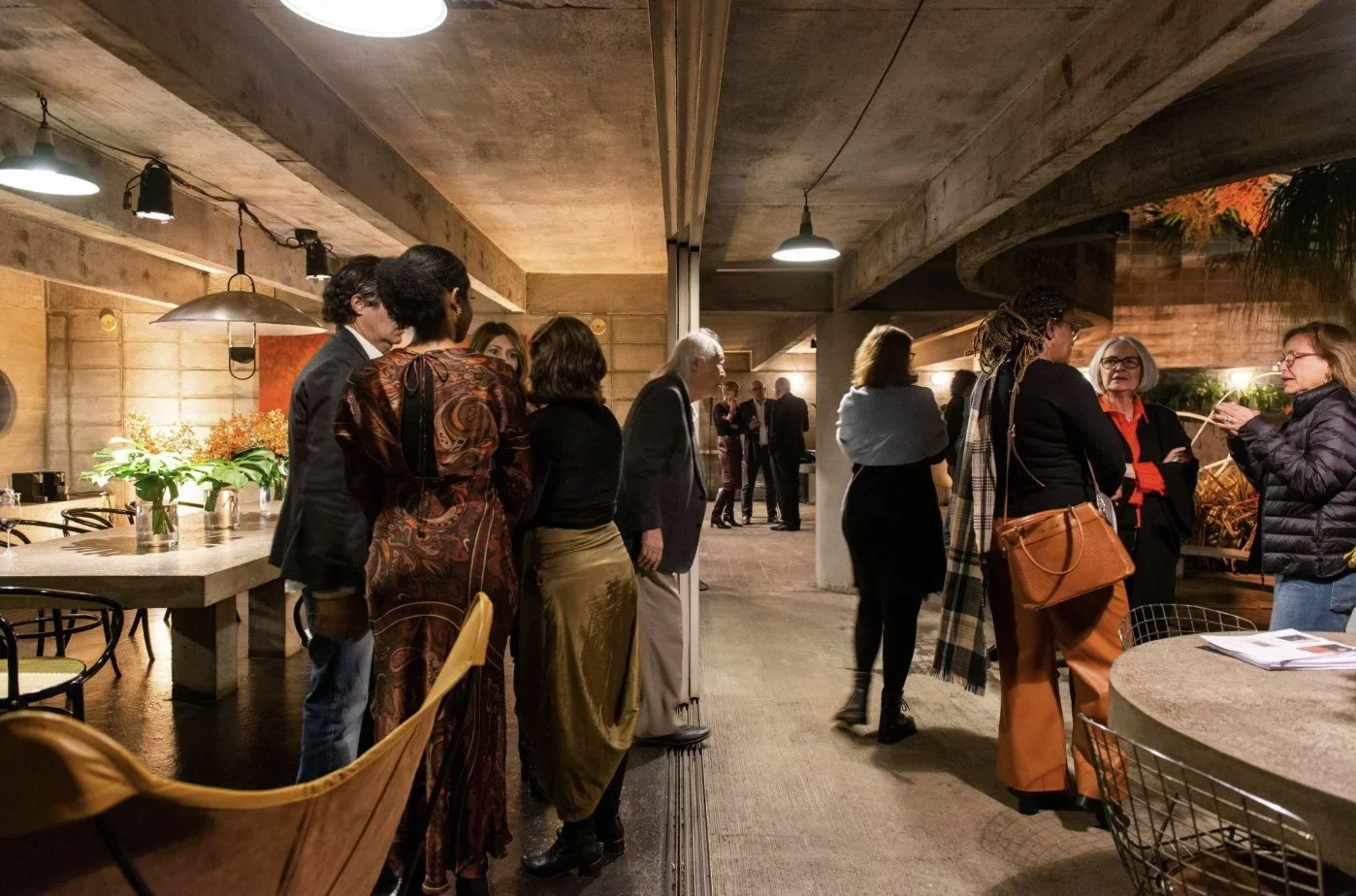 Pessoas conversando em um evento em um espaço com iluminação quente e decoração moderna.
