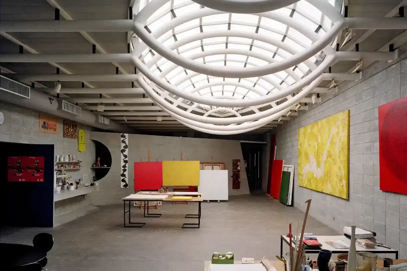 Interior de uma galeria de arte com pinturas coloridas na parede e instalações artísticas no espaço central.