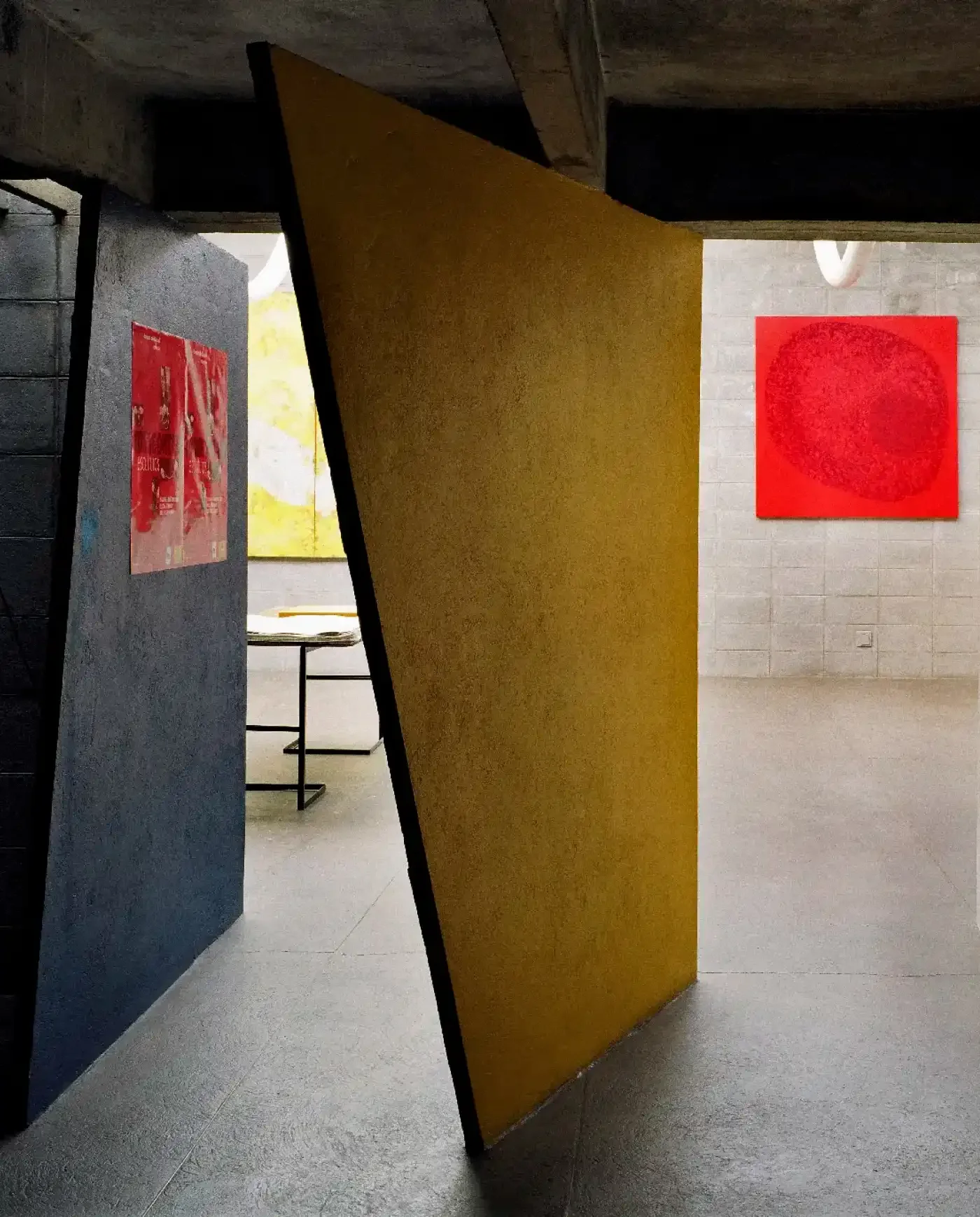 Imagem de uma instalação de arte com painéis de cores diferentes e obras de arte na parede, em um espaço com piso de azulejo e paredes de concreto.