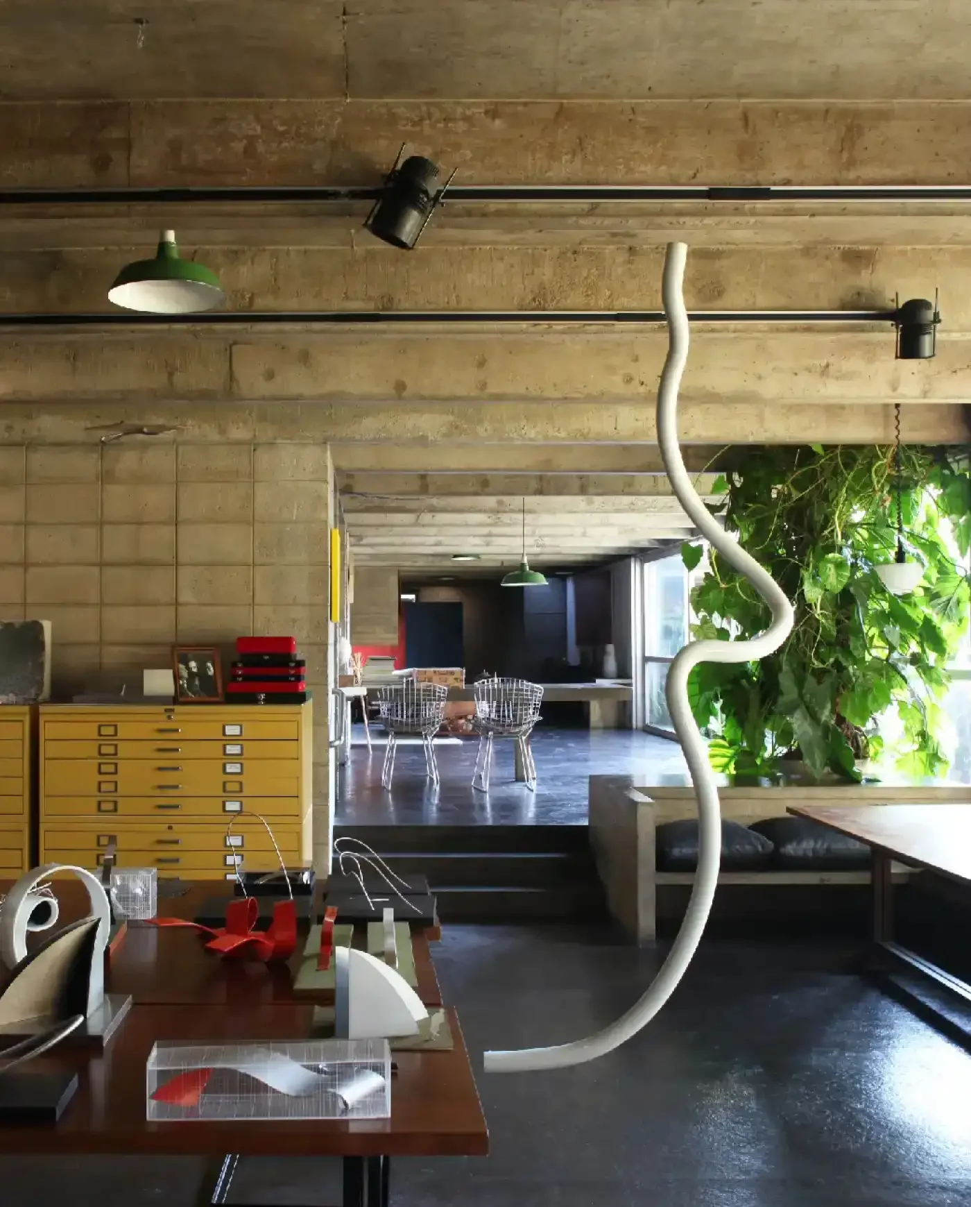 Interior de um espaço de trabalho com móveis sustentáveis e plantas, destaque para uma estrutura sinuosa branca ao lado de uma grande planta verde