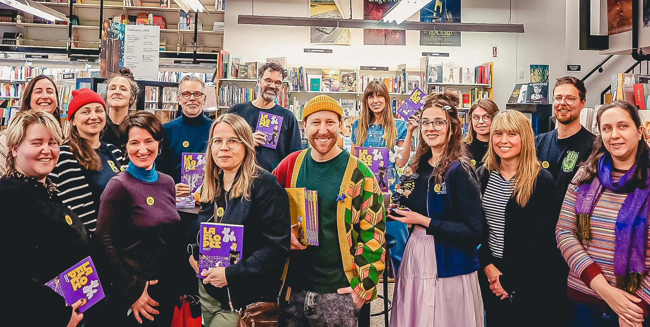 Groupe de personnes dans une librairie, tenant des livres et souriant, avec des étagères pleines de livres en arrière-plan.