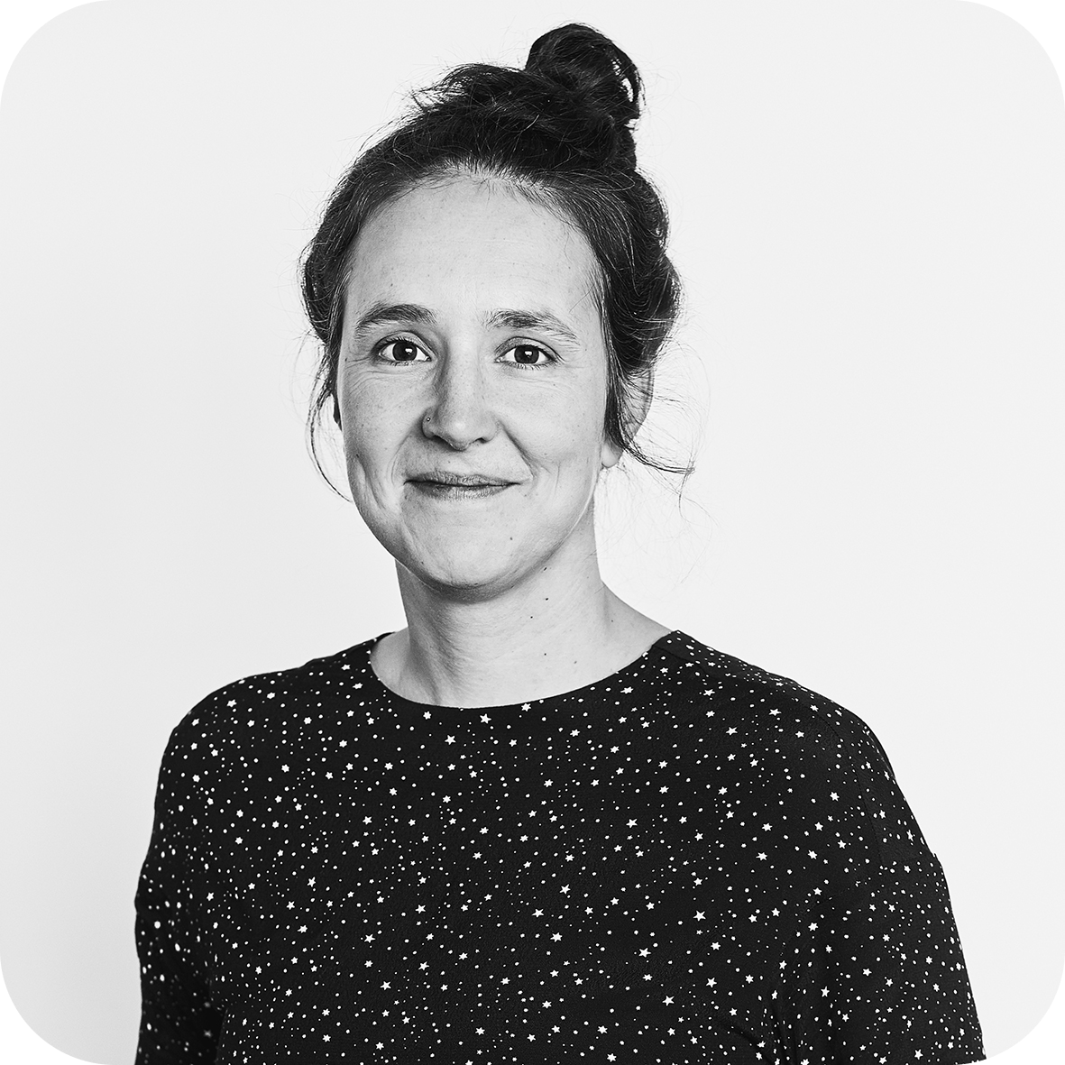 Portrait d'une femme souriante avec les cheveux relevés, portant un haut à motifs étoilés, en noir et blanc.
