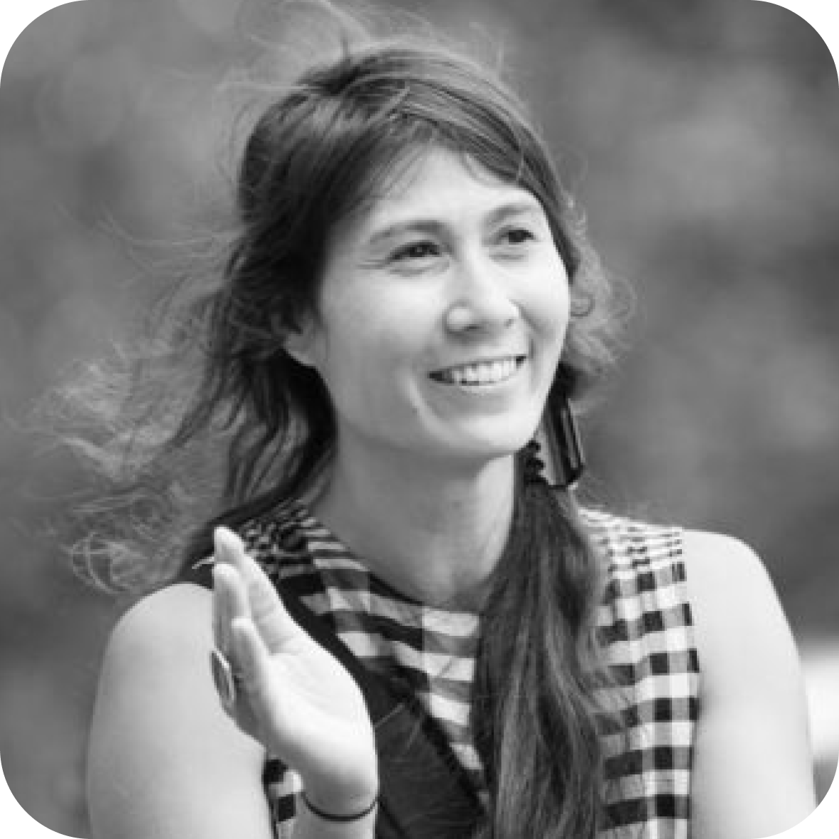 Une femme souriante avec des cheveux longs et ondulés, portant une chemise à carreaux, le tout en noir et blanc.