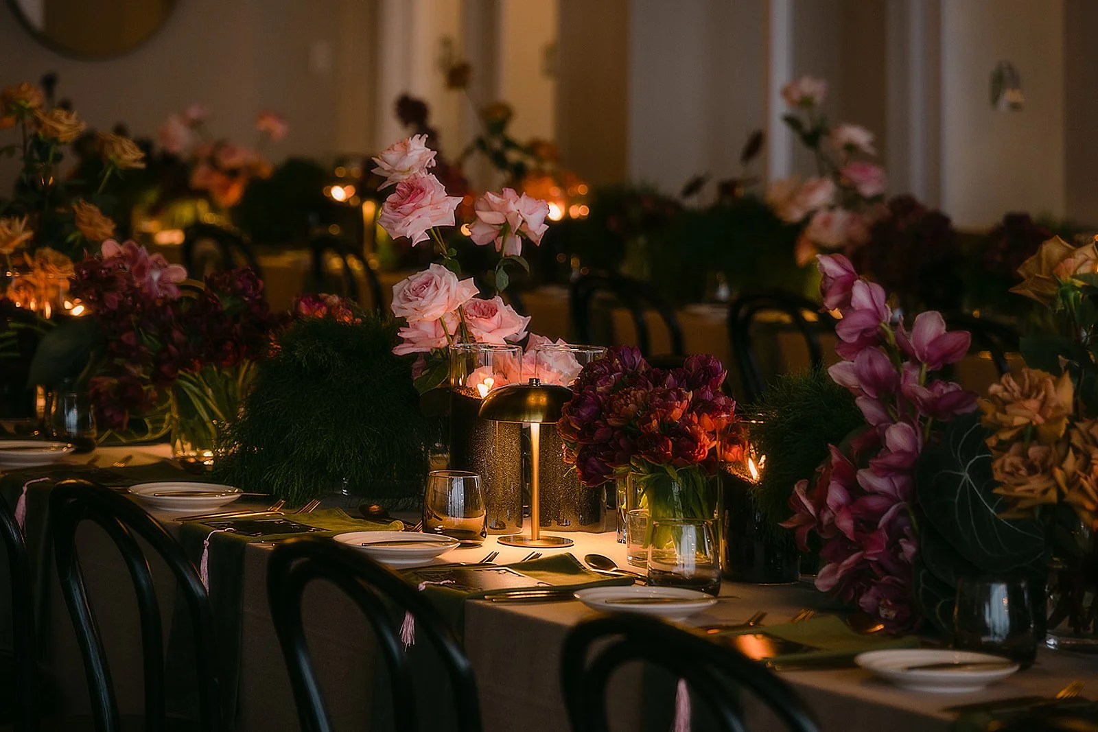 A beautifully decorated dining table with floral arrangements, candles, and elegant tableware in a dimly lit setting, likely for a special event or celebration.