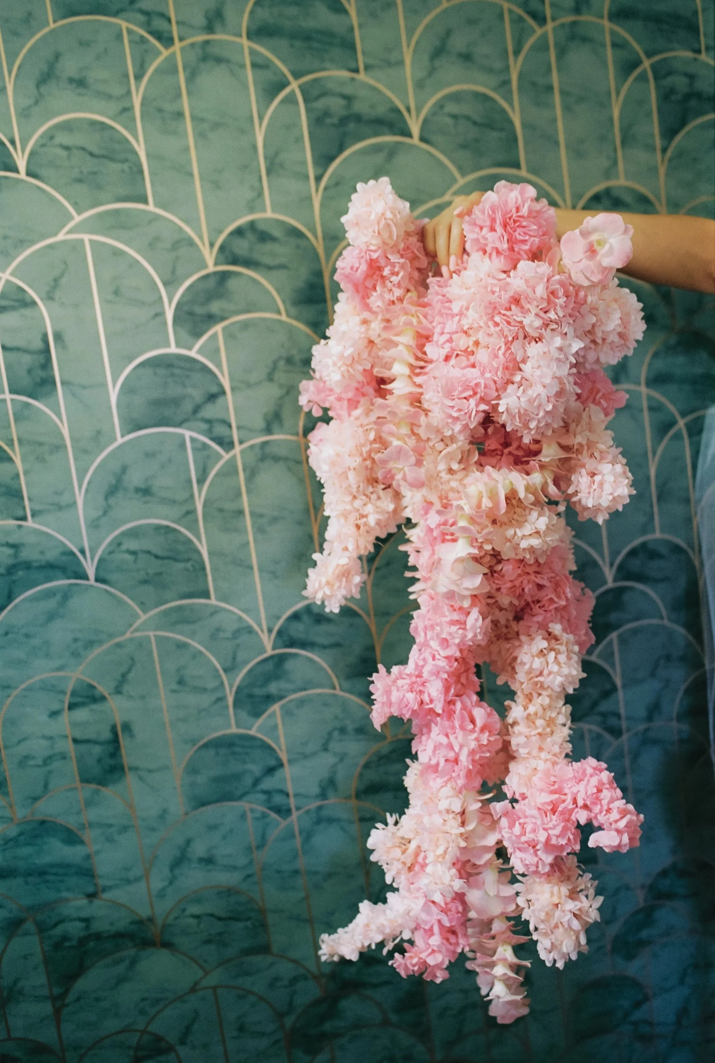 A pink flower arrangement hanging against a teal patterned wall.