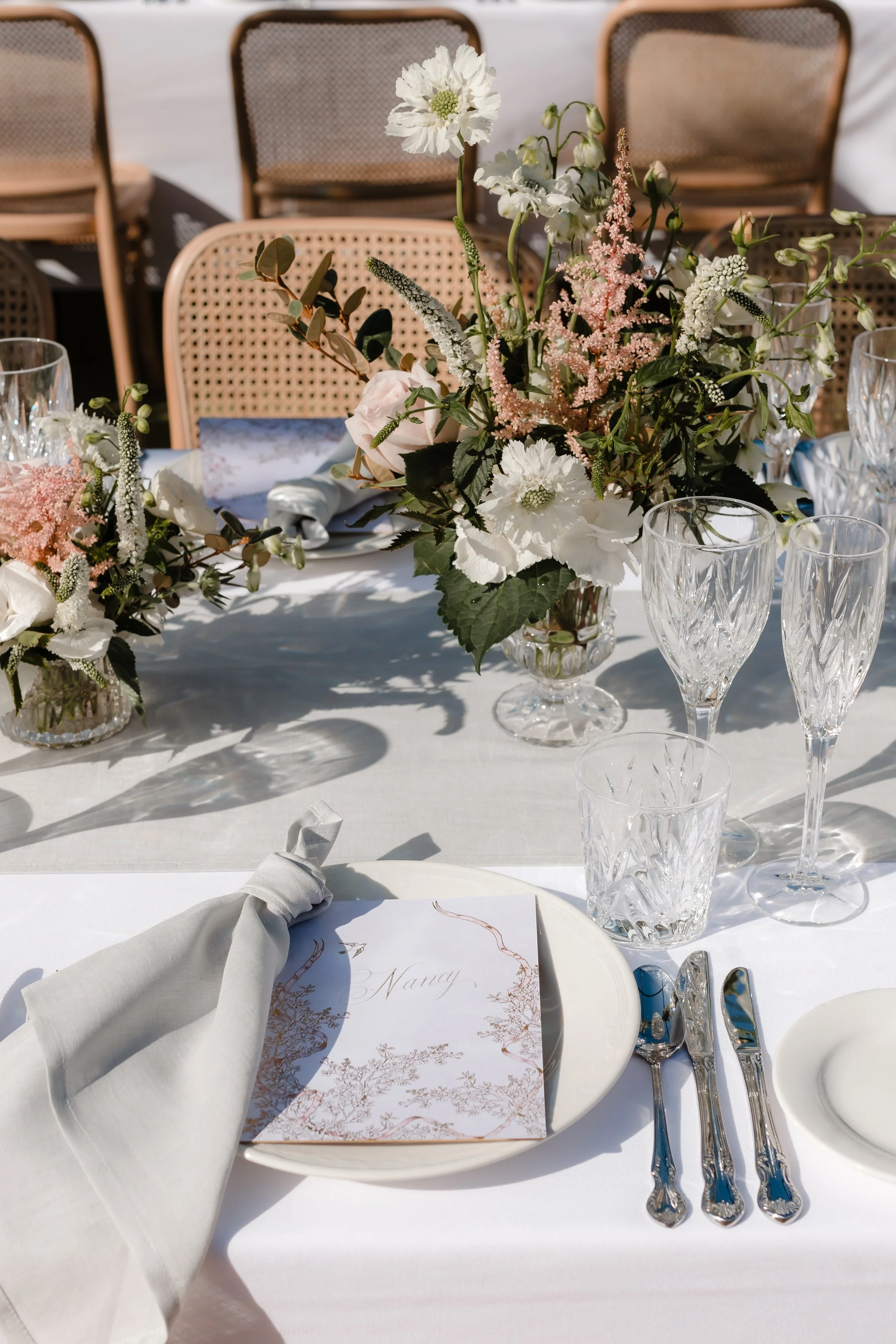 Elegant dining table setup with floral centerpiece, wine glasses, and place setting with a napkin and menu card.